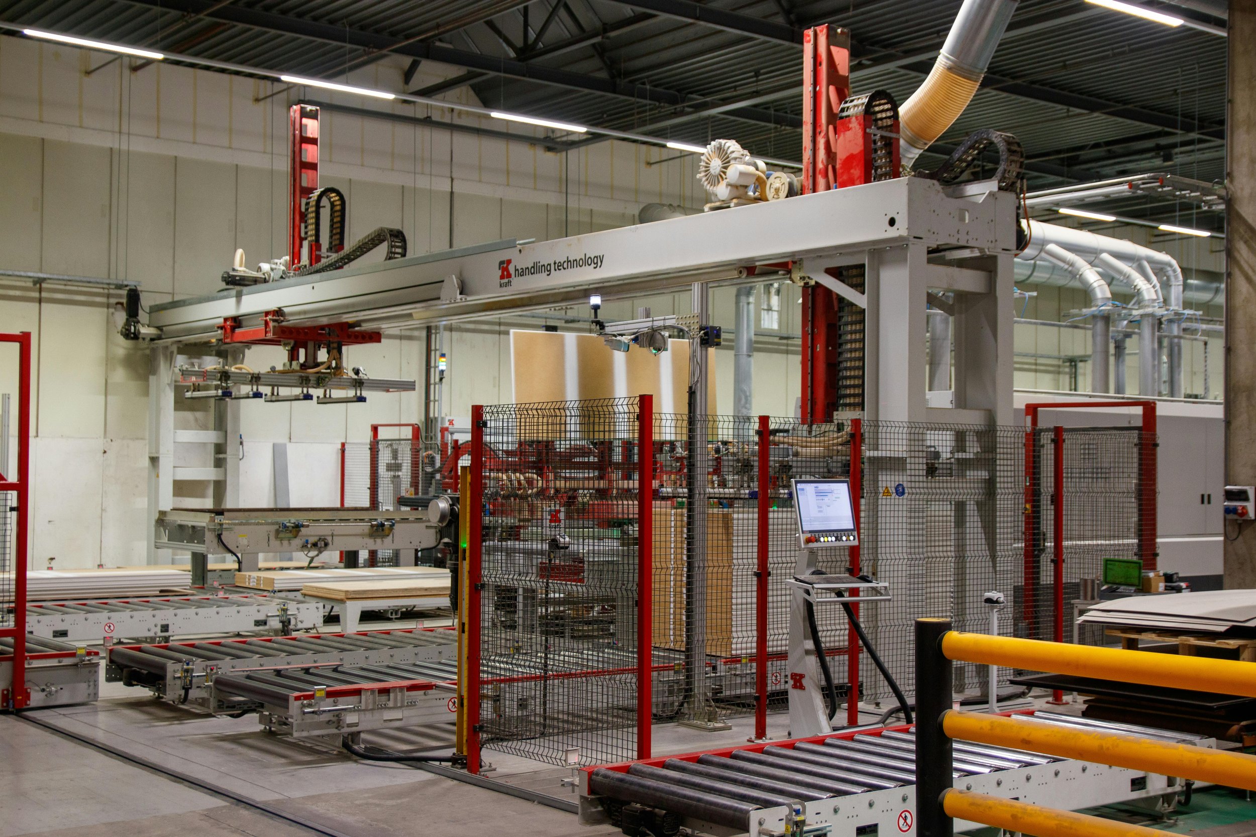 Industrial machine in a manufacturing plant with a computer control panel, conveyor system, and safety fencing.