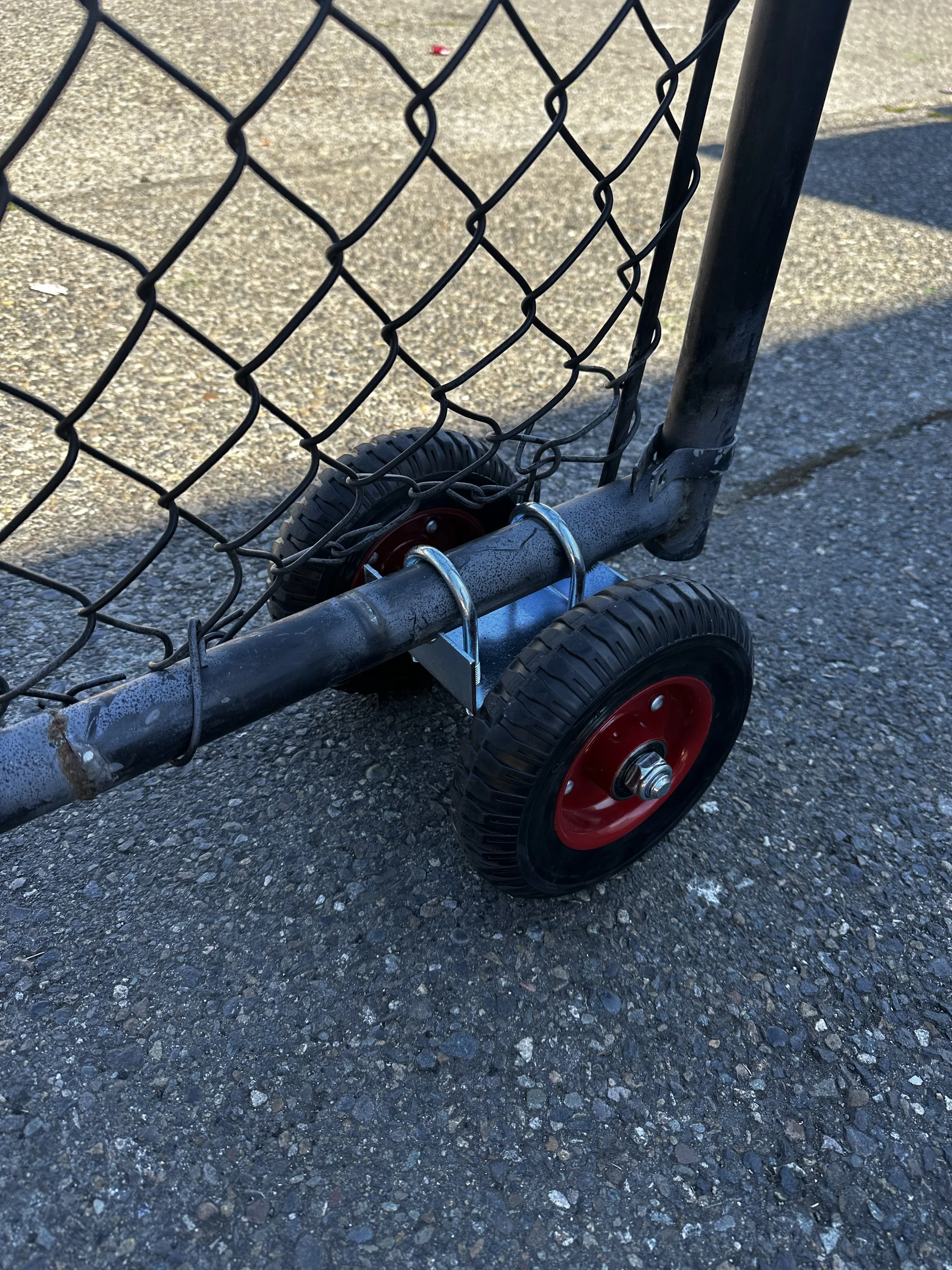 Close-up of a small shopping cart with black wheels and a black metal frame, on rough asphalt ground.