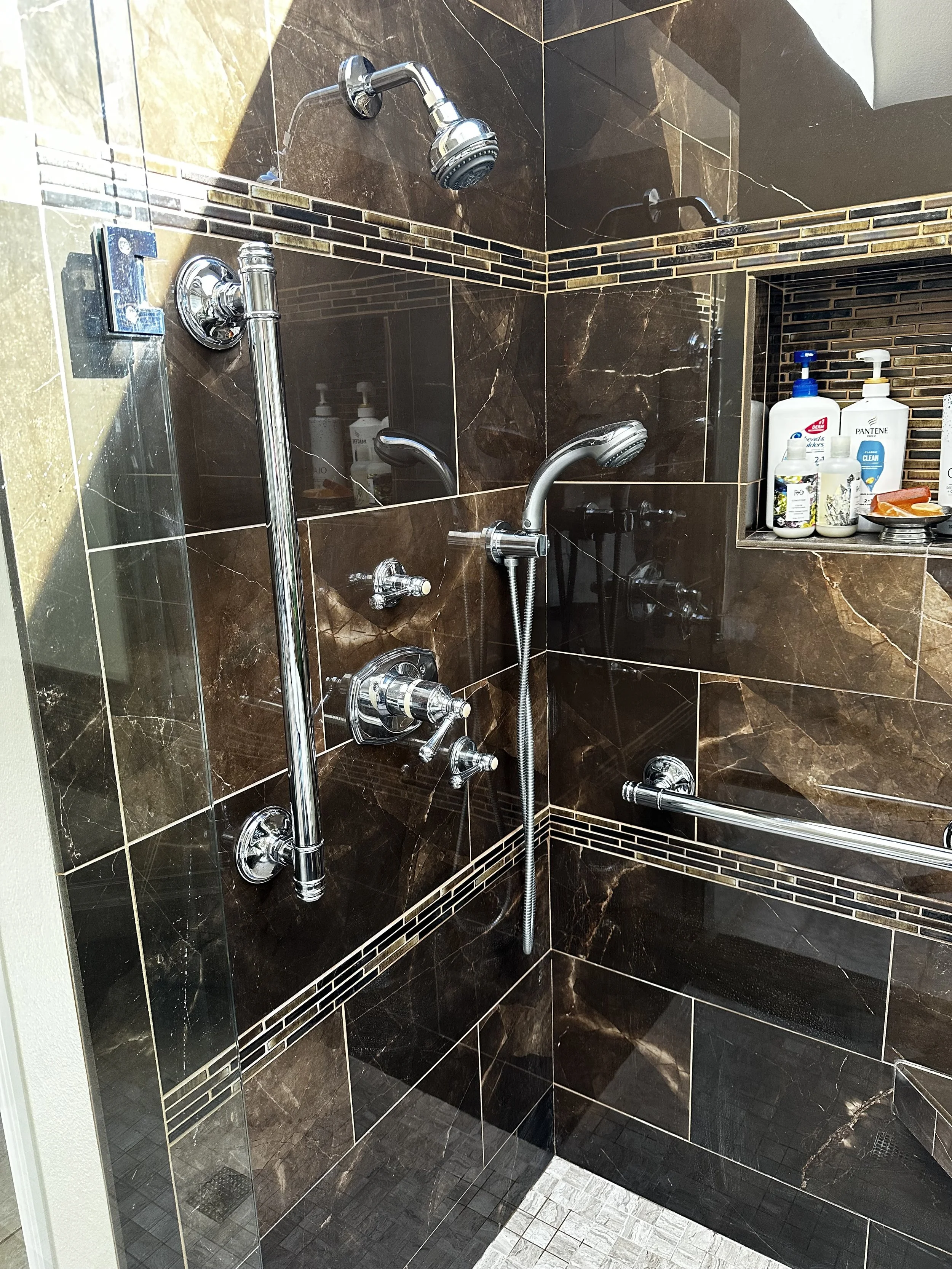 Showers with multiple shower heads, grab bars, and toiletries on a tiled wall.