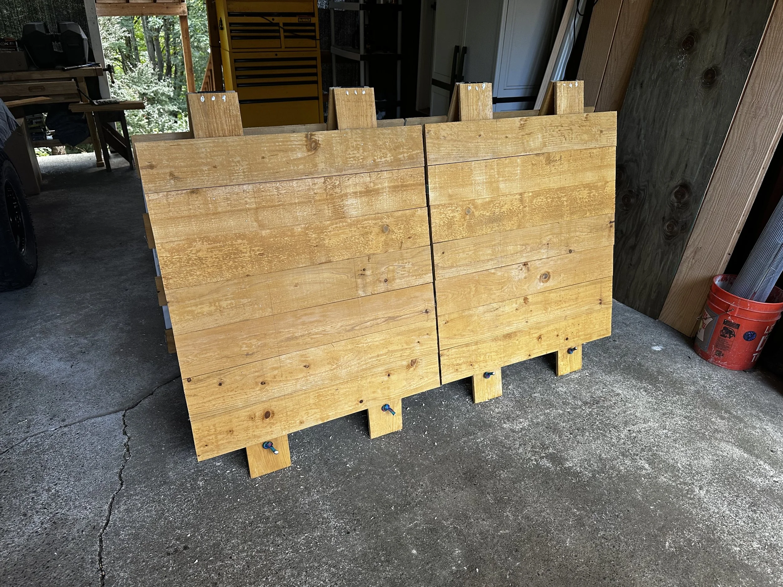 Two wooden pallets stand upright in a garage, leaning against a wall, with some visible hardware and tools in the background.