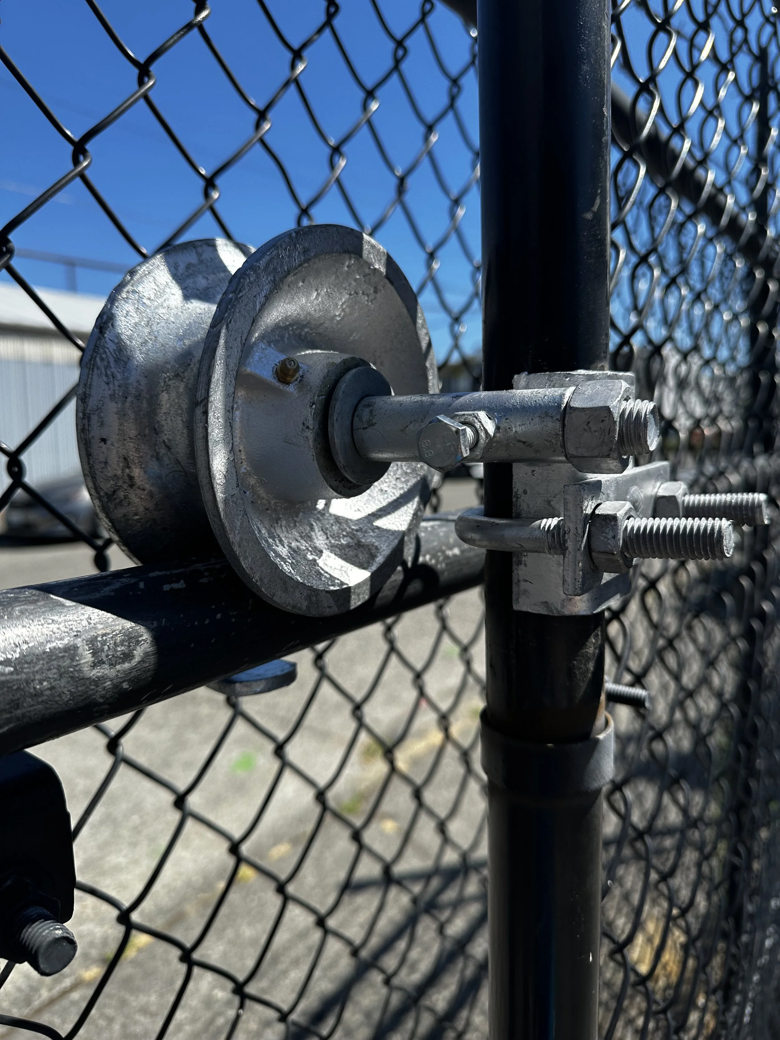 Close-up of a fence latch mechanism attached to a chain-link fence with a blue sky in the background.