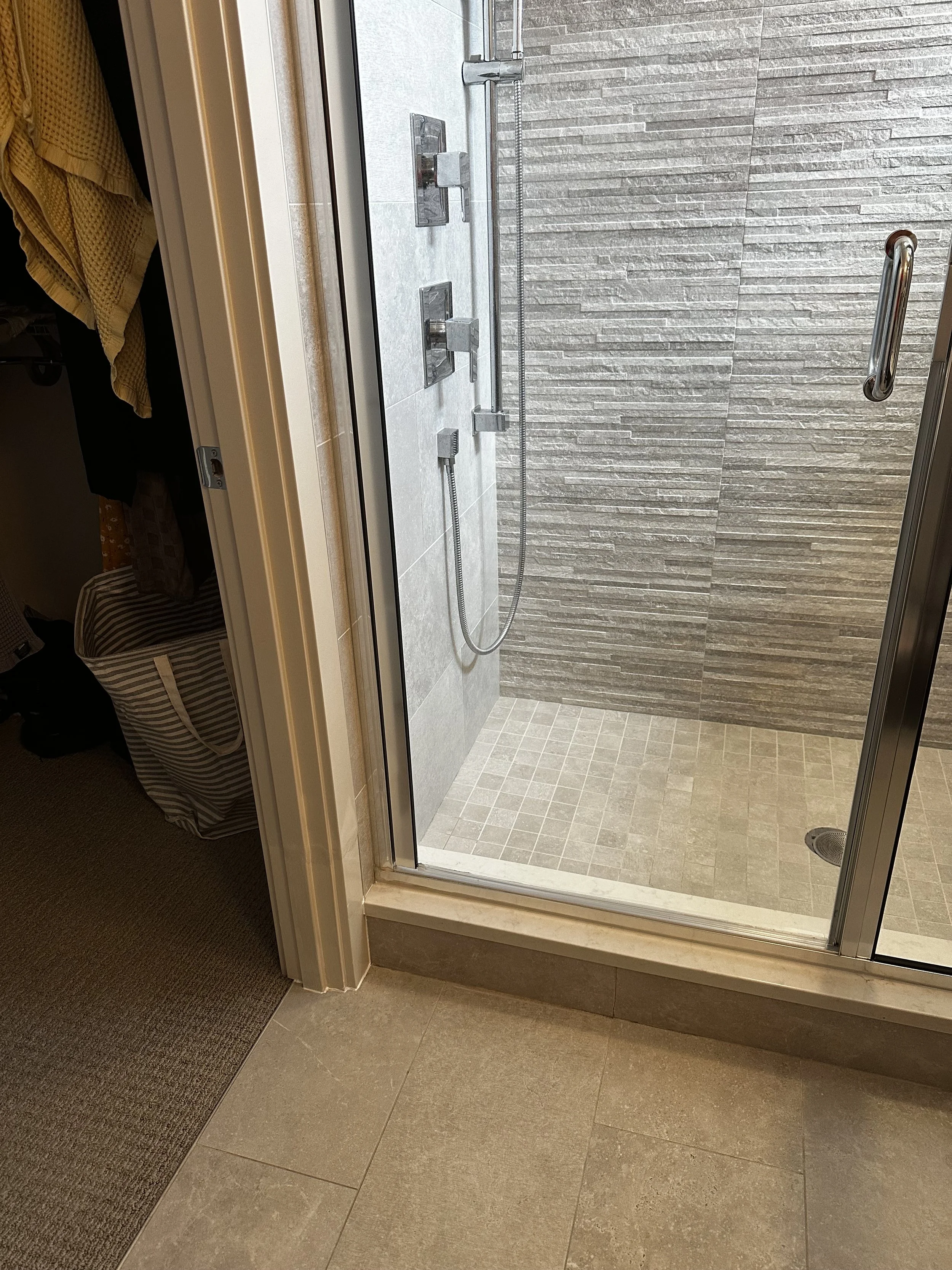 Modern shower with glass door, gray tiled walls, and a built-in grab bar.