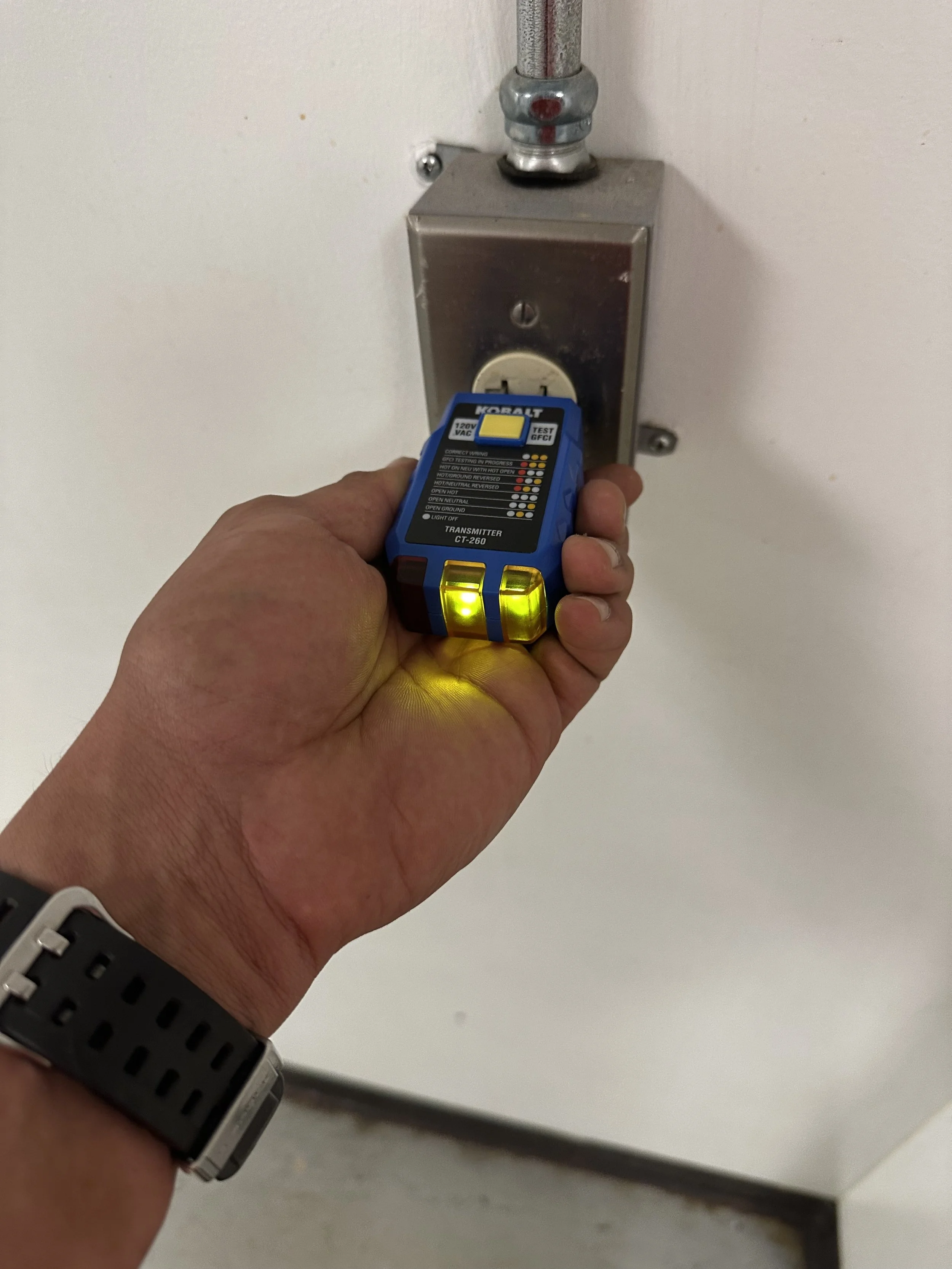 Person testing an electrical outlet with a non-contact voltage tester in a wall-mounted metal electrical box.