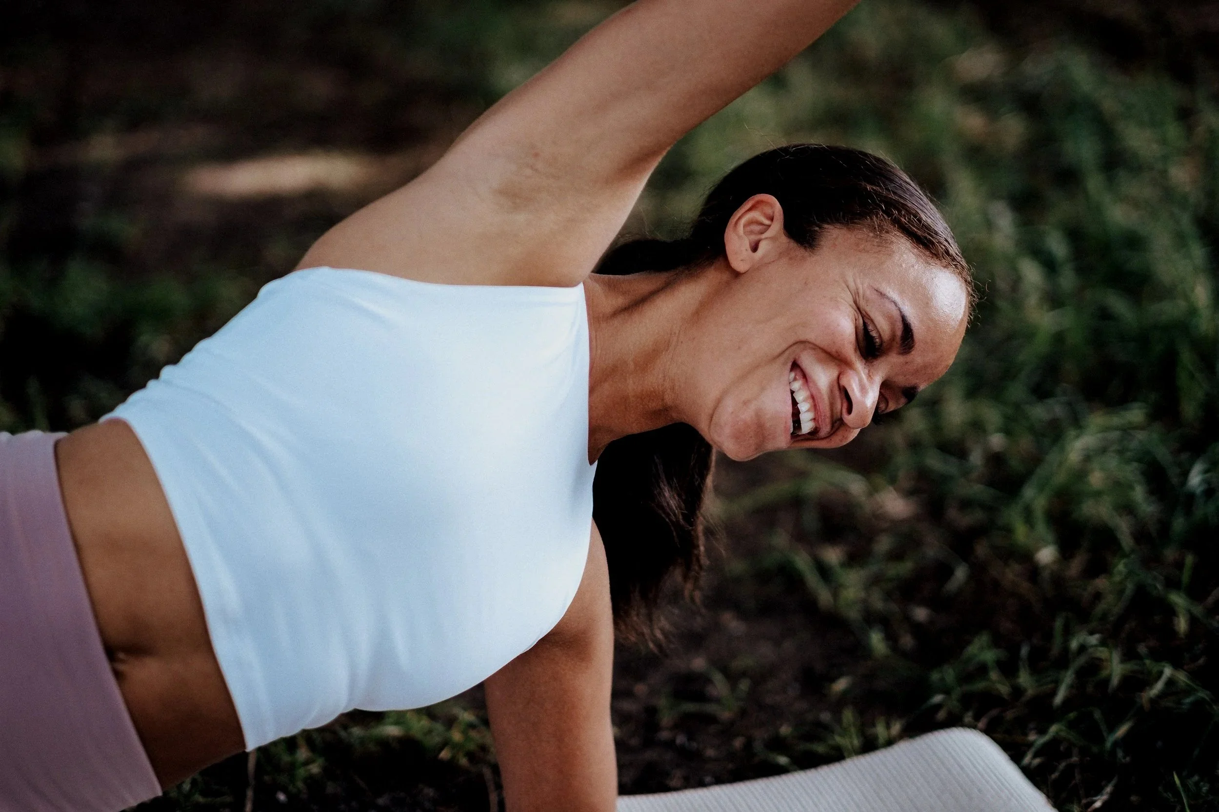Frau macht Yoga im Freien, lacht und liegt auf der Erde.