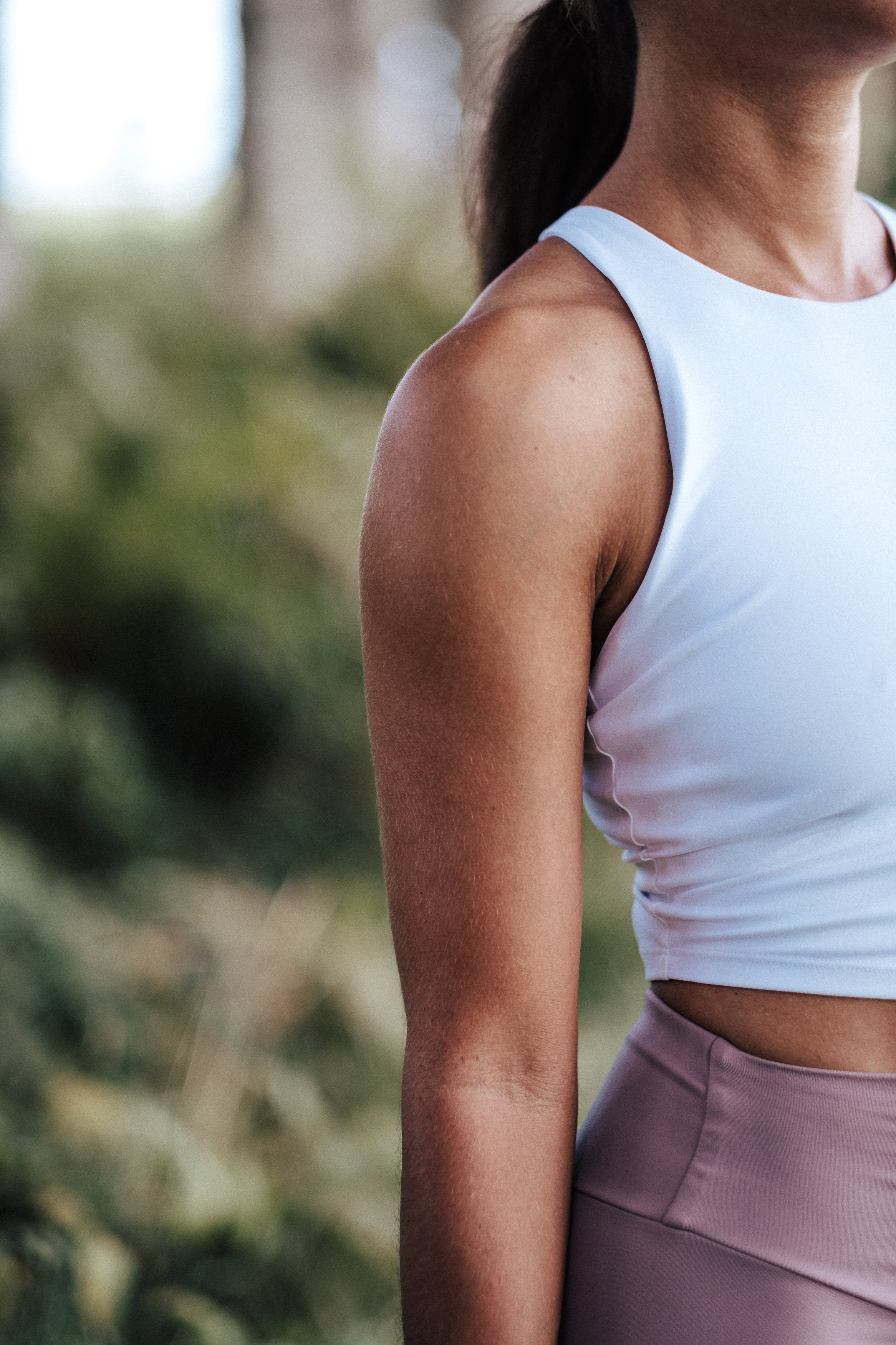 Nahaufnahme eines weiblichen Armes, Schulter und Bauch in sportlicher Kleidung, im Freien.