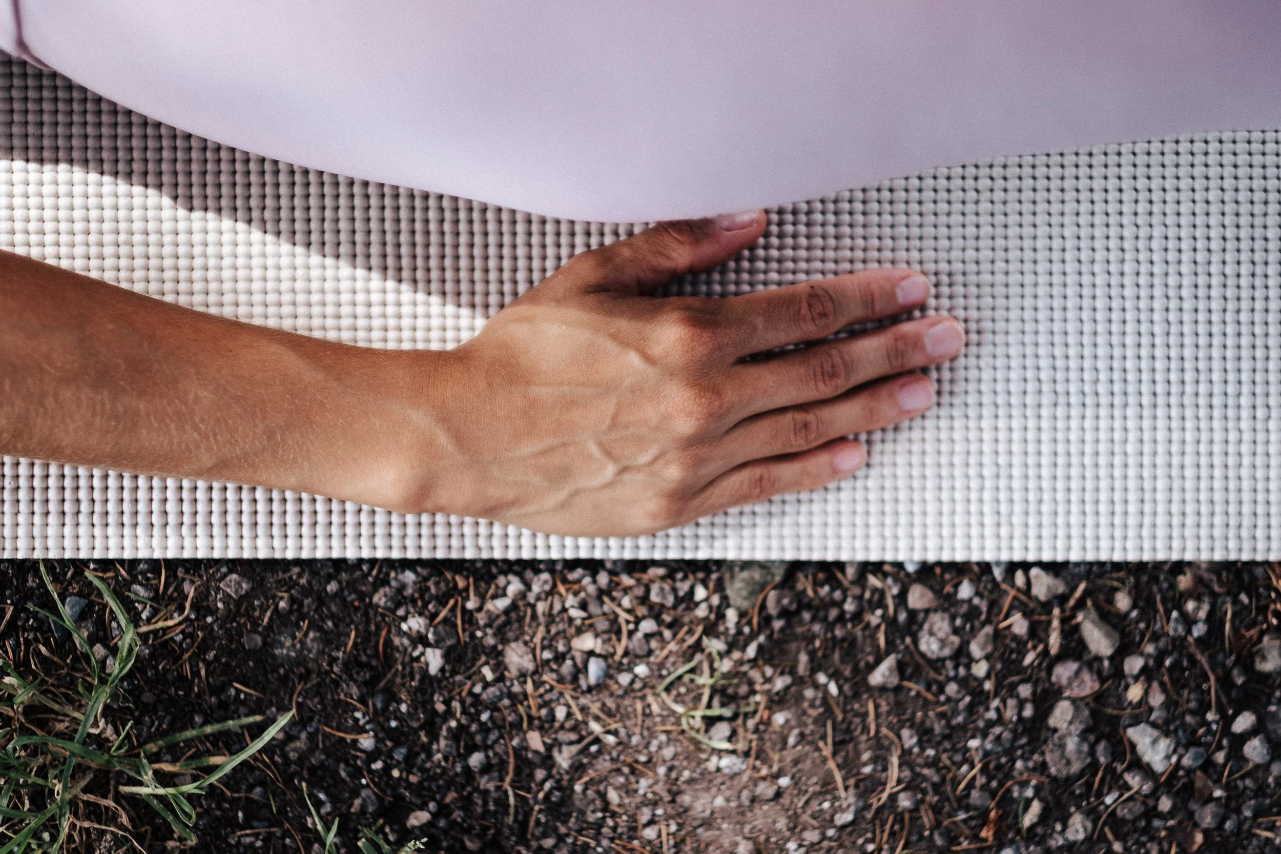 Hand, die eine Yoga-Matte auf Erde auslegt.