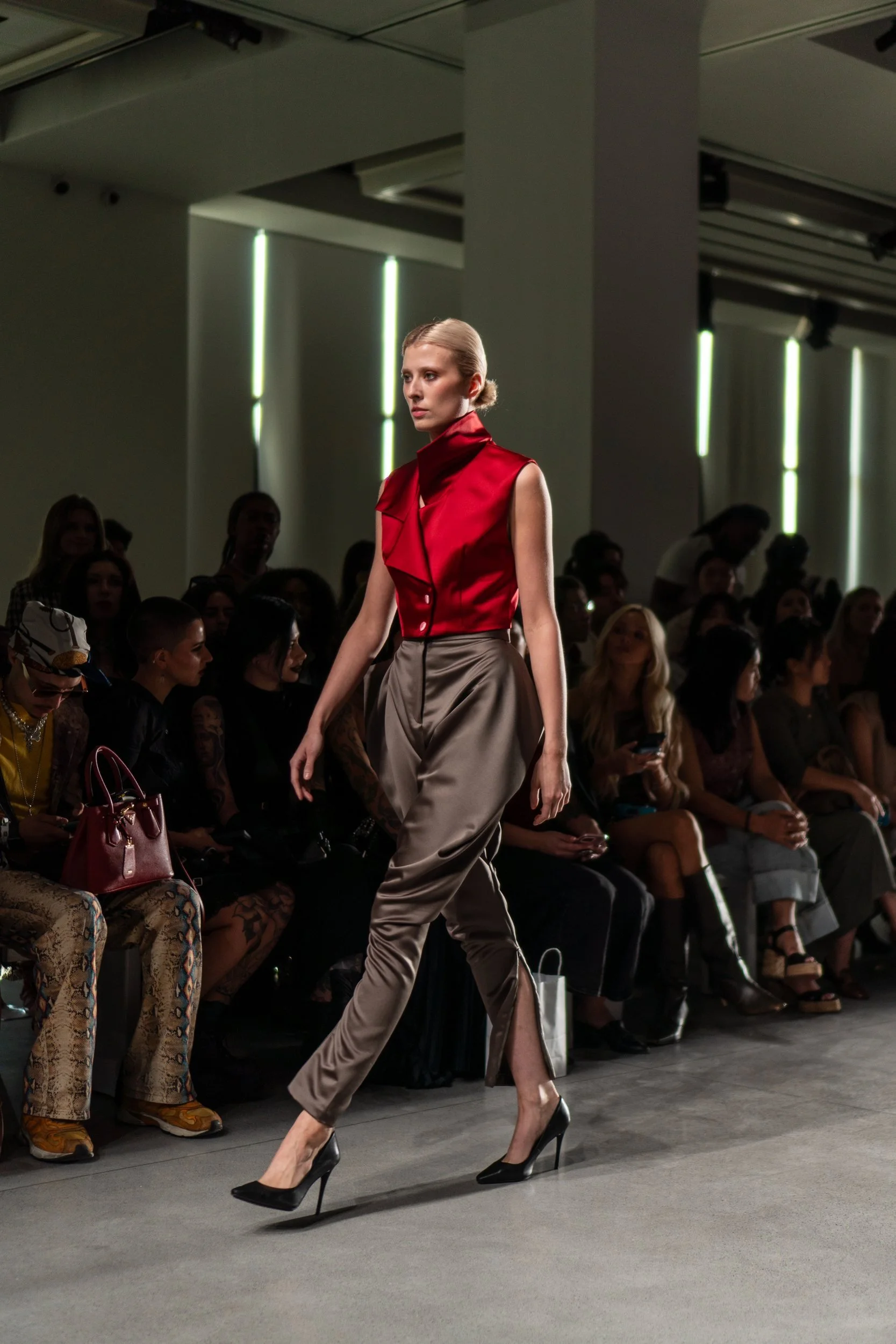 Model in a red top and gray trousers walking down a runway