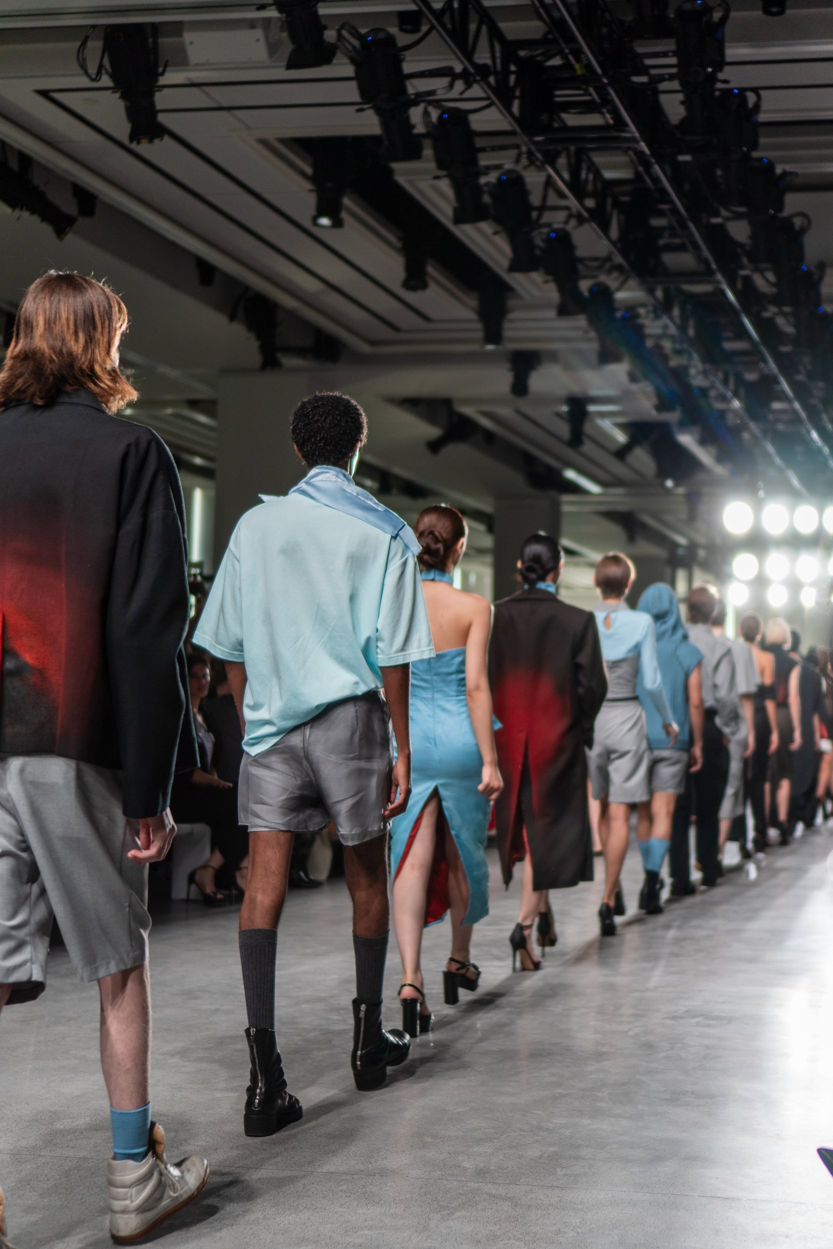 Models walking away in a line beneath runway lights