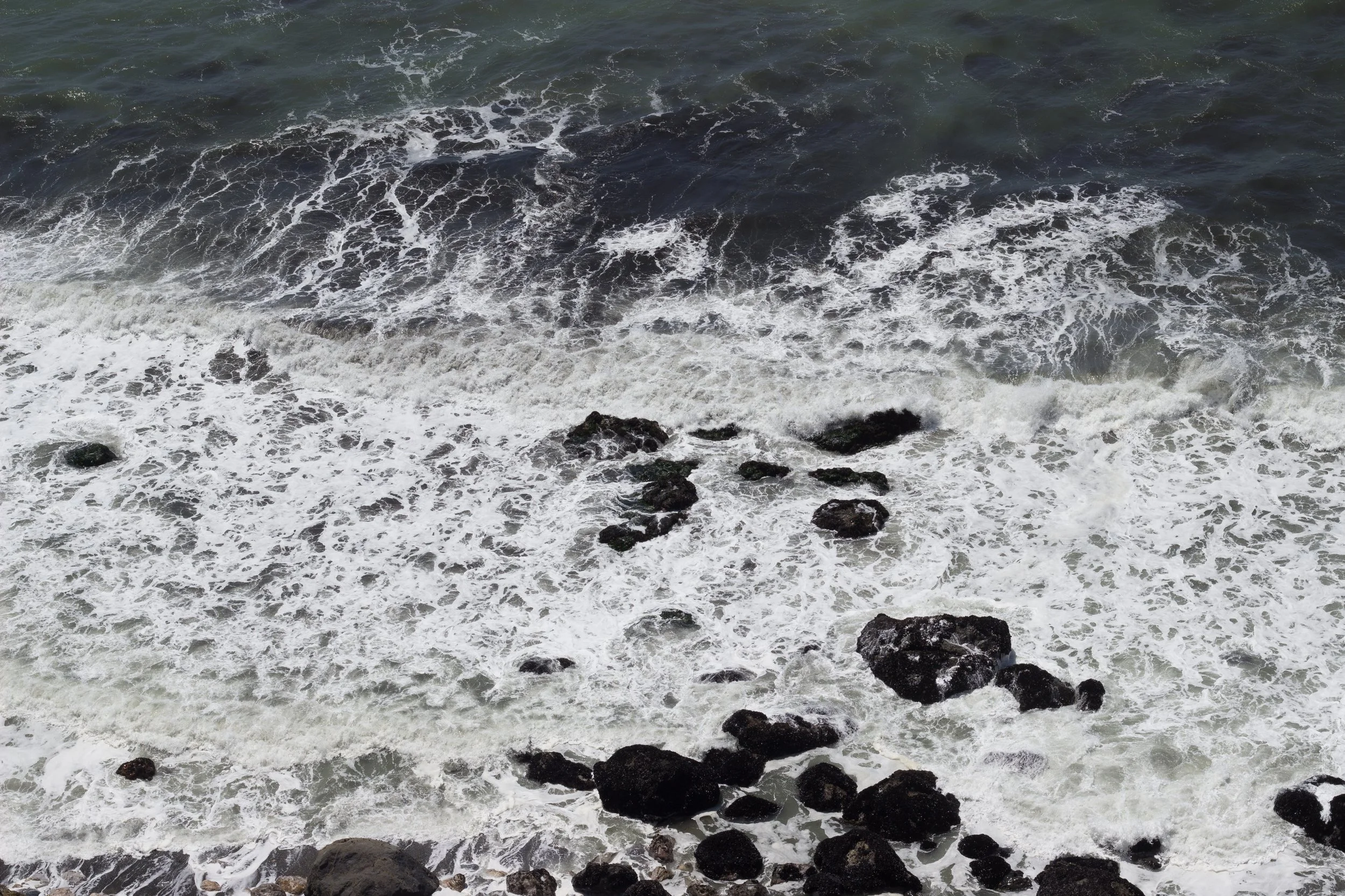 Ocean foam and dark rocks seen from above