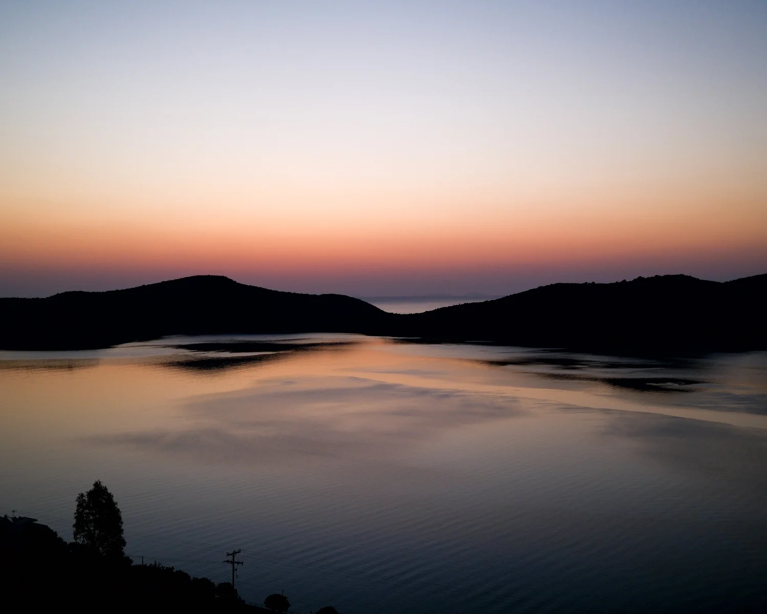 Fog flowing between dark hills beneath a pastel dusk sky