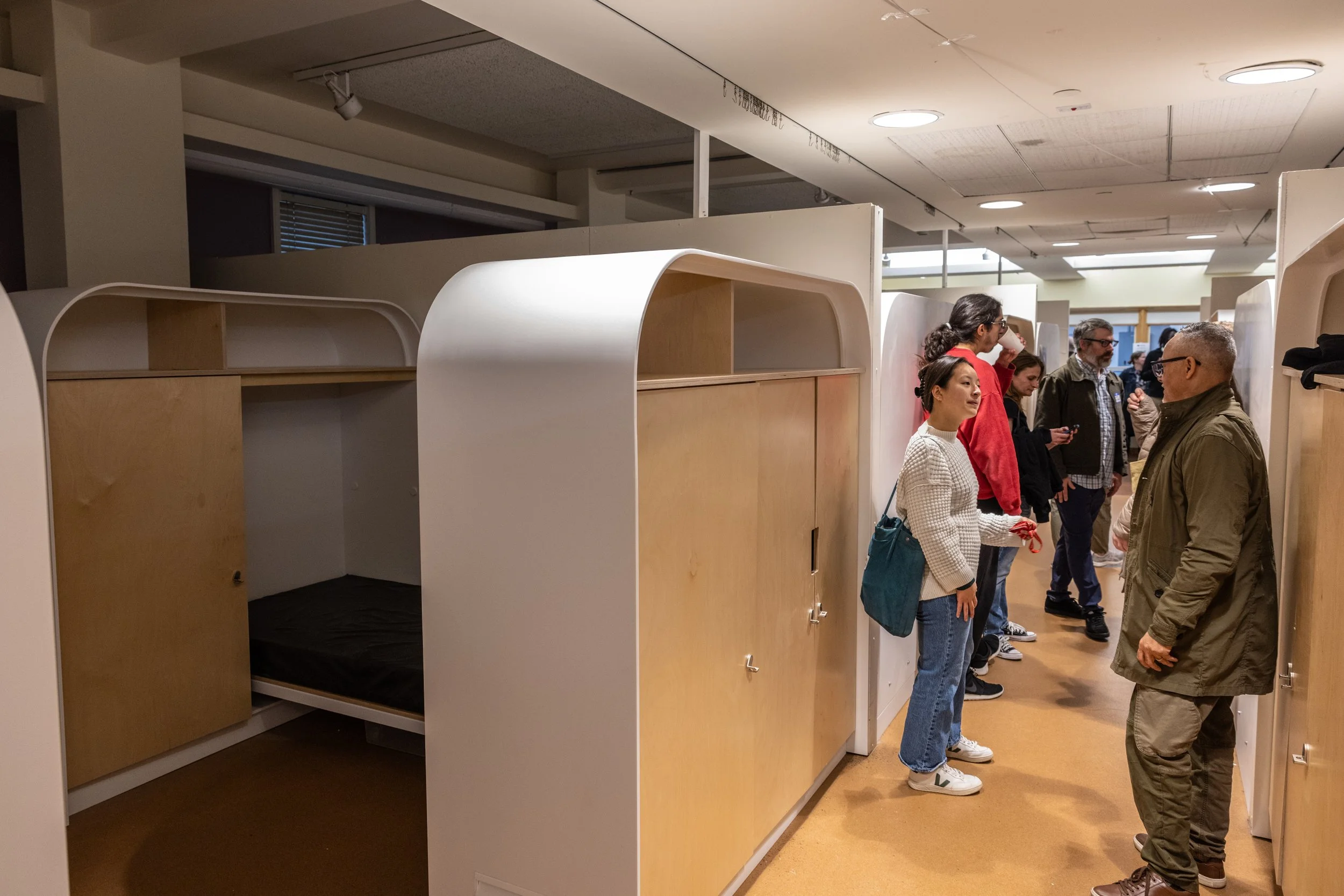 People touring a furniture store with modular wooden and white beds and wardrobes.