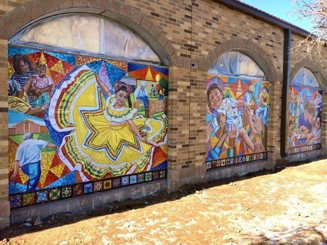 Colorful mural depicting dancers, musicians, and cultural scenes on the exterior of a brick building.
