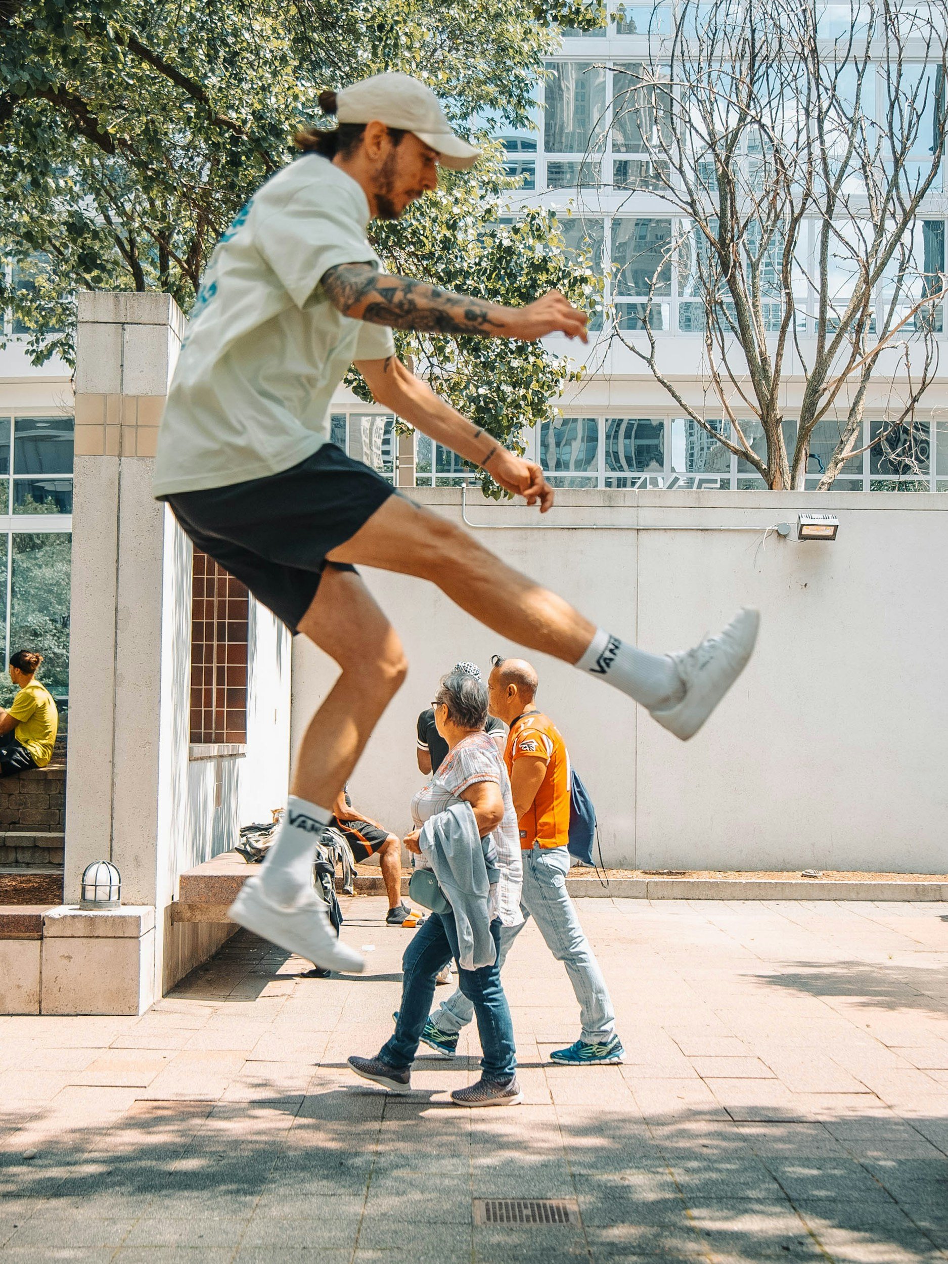 A man jumping in the air with a city background, passing over people walking on the sidewalk.