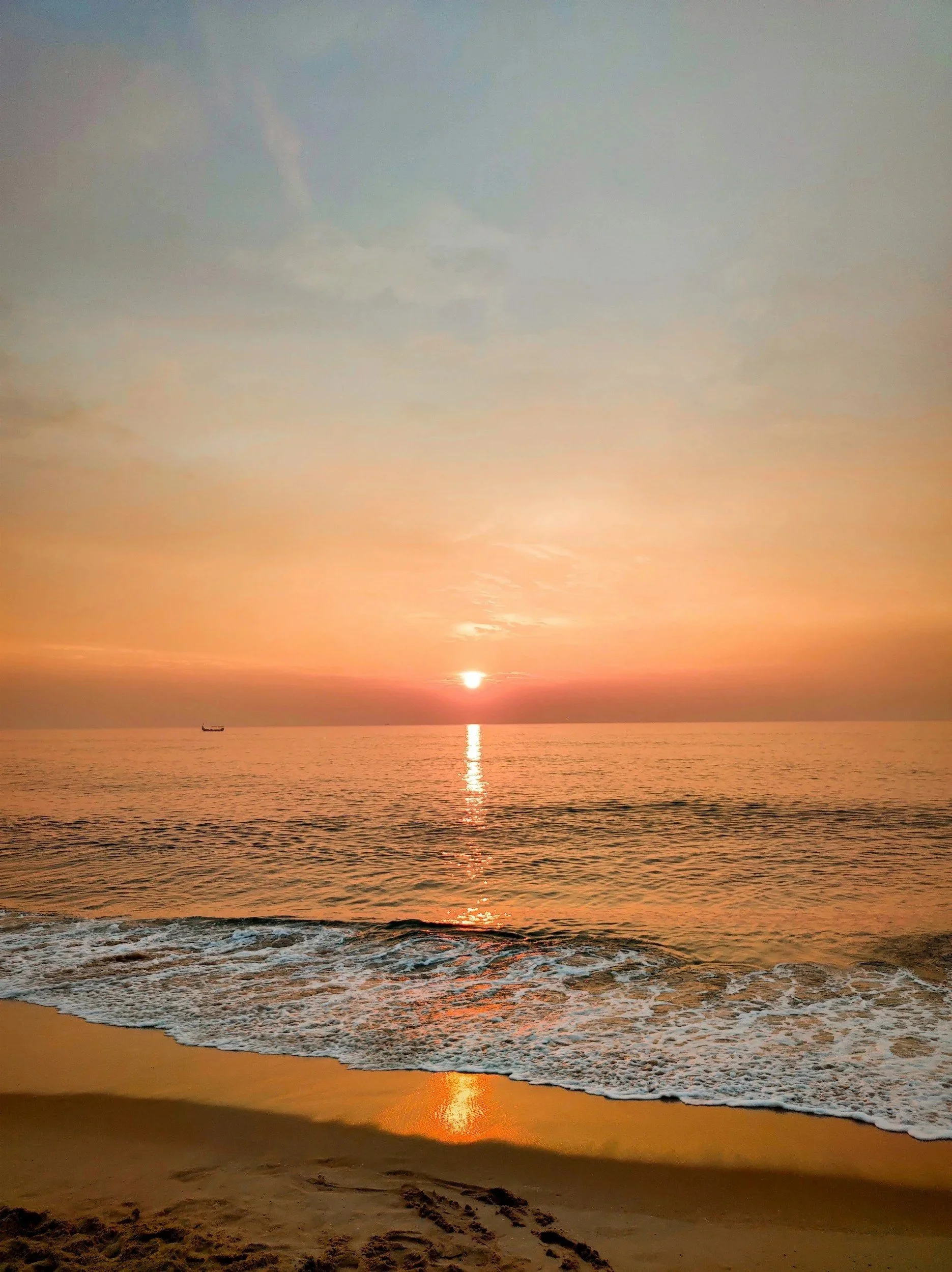 A sunset over the ocean, viewed from a sandy beach with gentle waves.