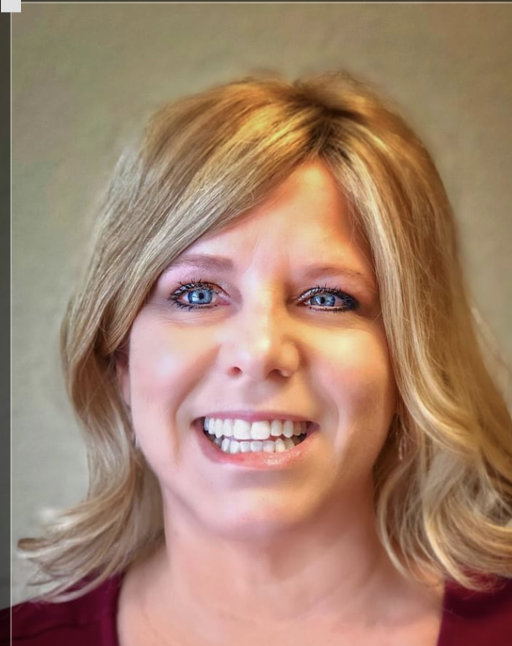 Close-up of a woman with blonde hair and blue eyes smiling against a neutral background.
