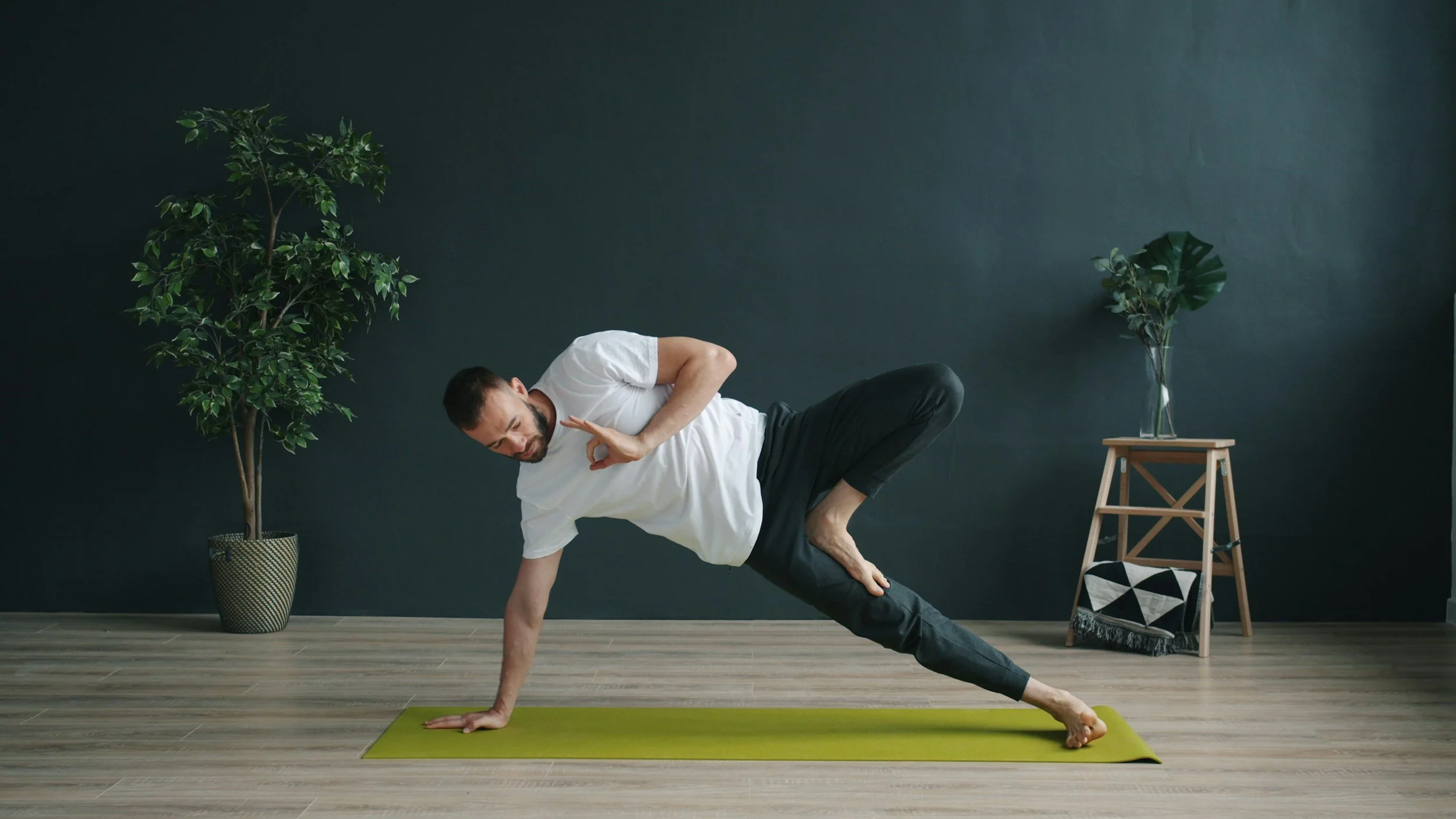 Light-skinned man practicing modified side plank pose on yellow yoga mat in minimalist room
