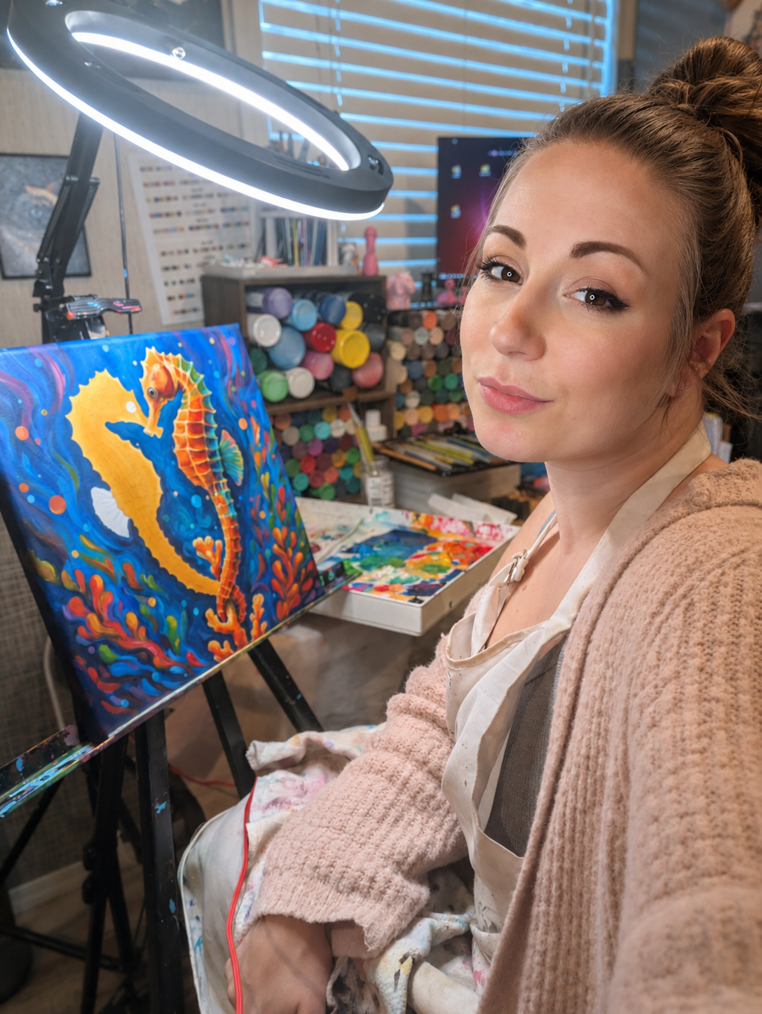 A woman painting a colorful underwater scene with a seahorse on a canvas in an art studio.