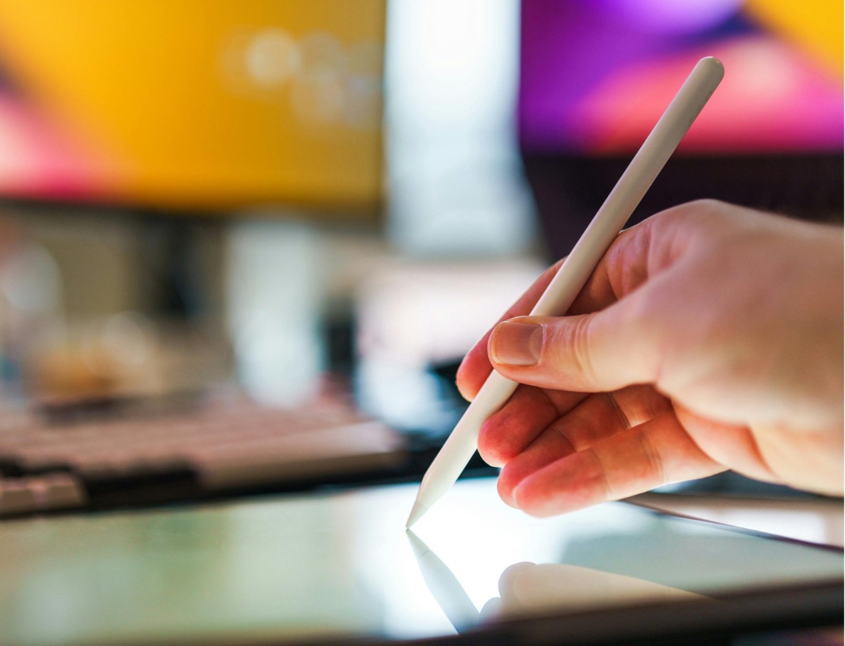 A hand holding a white stylus touching a touchscreen device.