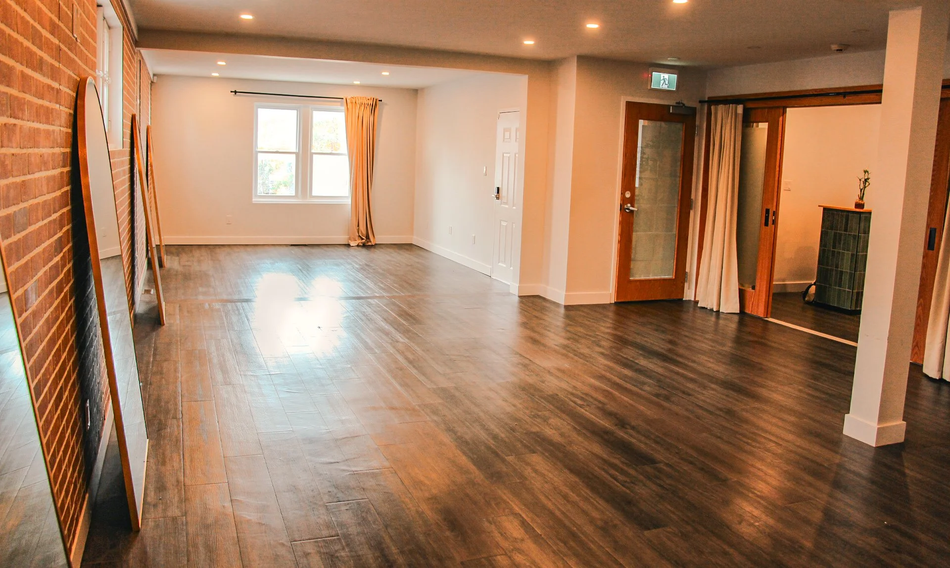 Empty interior room with wood floor, white and brick walls, window with curtains, and doorways with curtains.