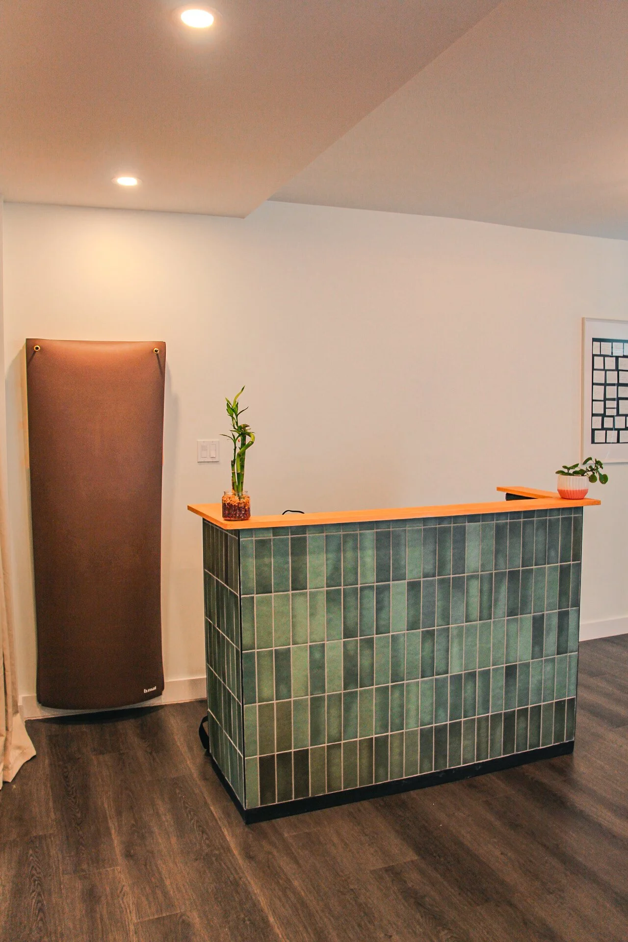 A modern interior with a green tiled bar counter, a bamboo plant in a glass container, a small potted plant, and ceiling lights.