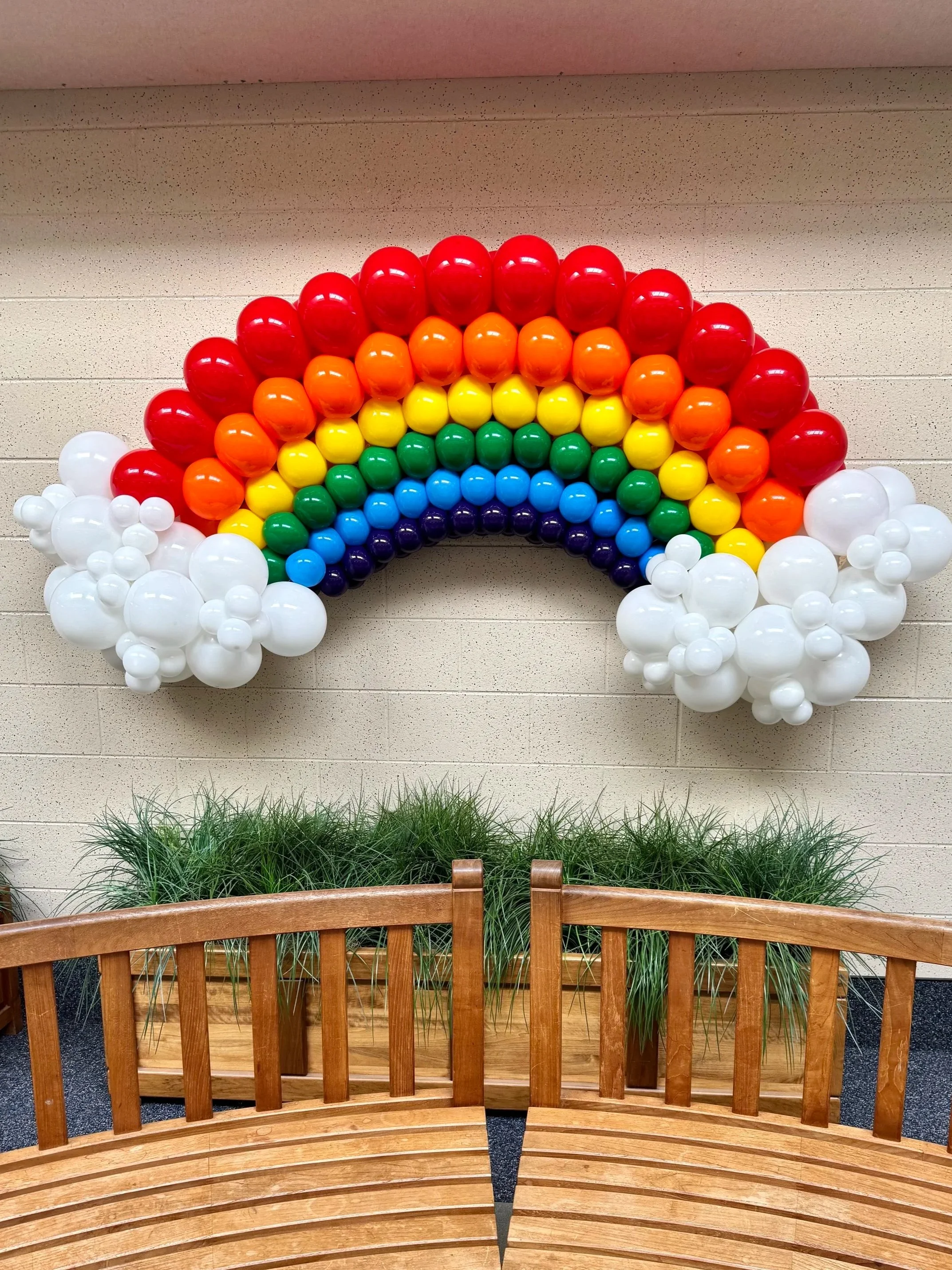 Balloon rainbow installation with clouds and grass, with two wooden benches in front.
