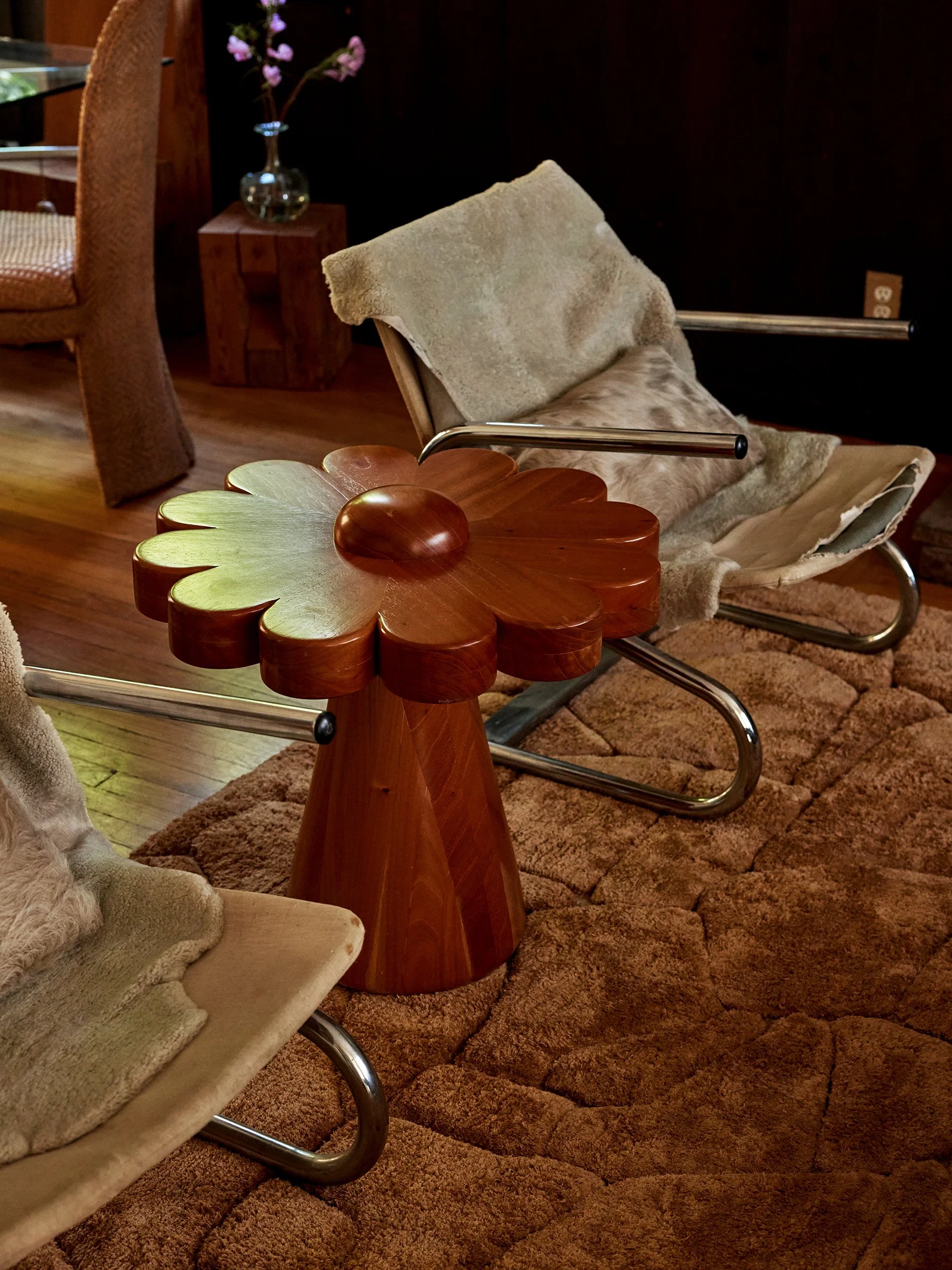Mid-century modern living room with two lounge chairs, a flower-shaped wooden side table, and a dark wall with electrical outlets.