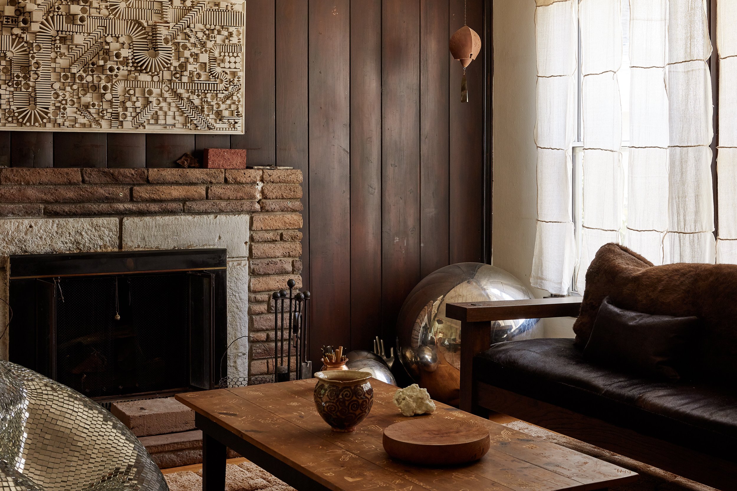Living room with brick fireplace, wooden wall, white curtains, and bronze sphere decorative objects.