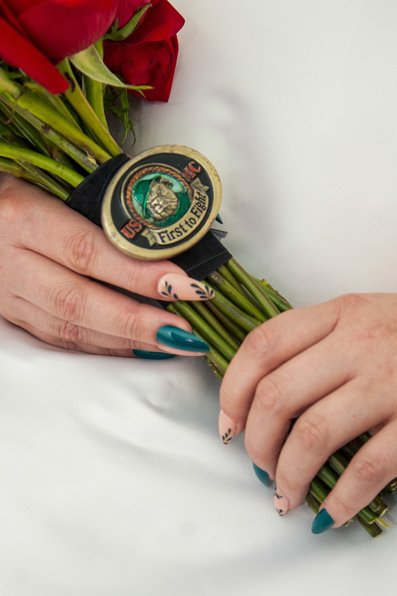 A person holding a bouquet of red roses wrapped with a 'First to Fight' military badge.