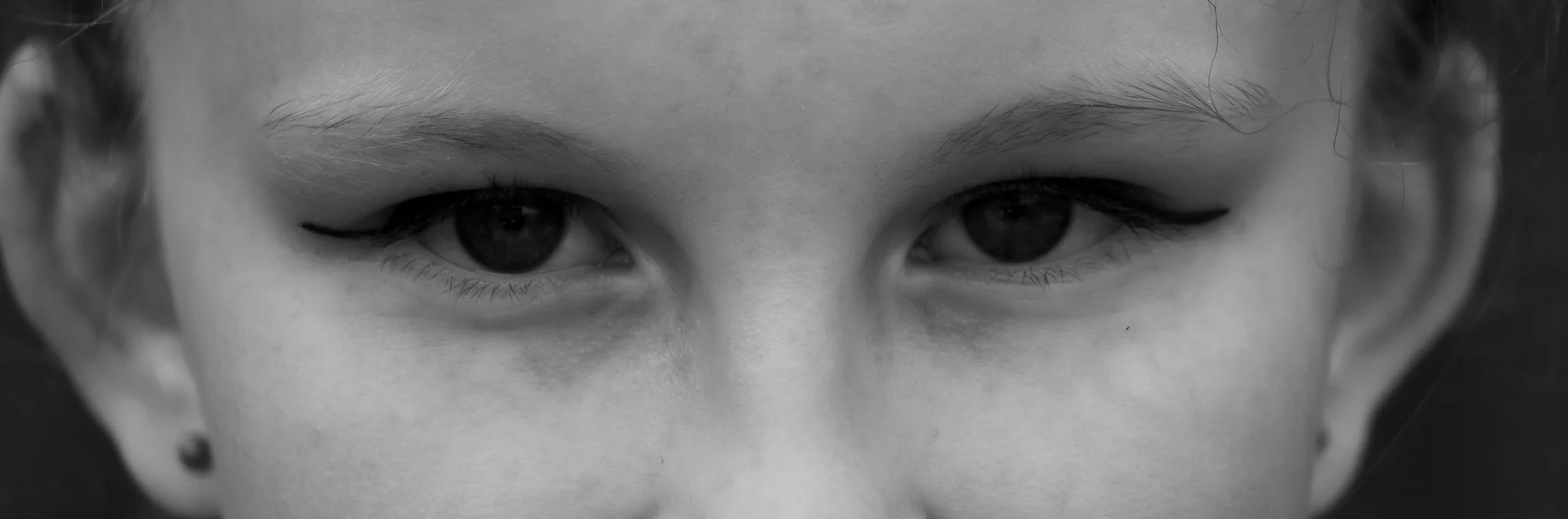 Close-up black and white photo of a person's face focusing on their eyes, with eyeliner applied and short hair visible.