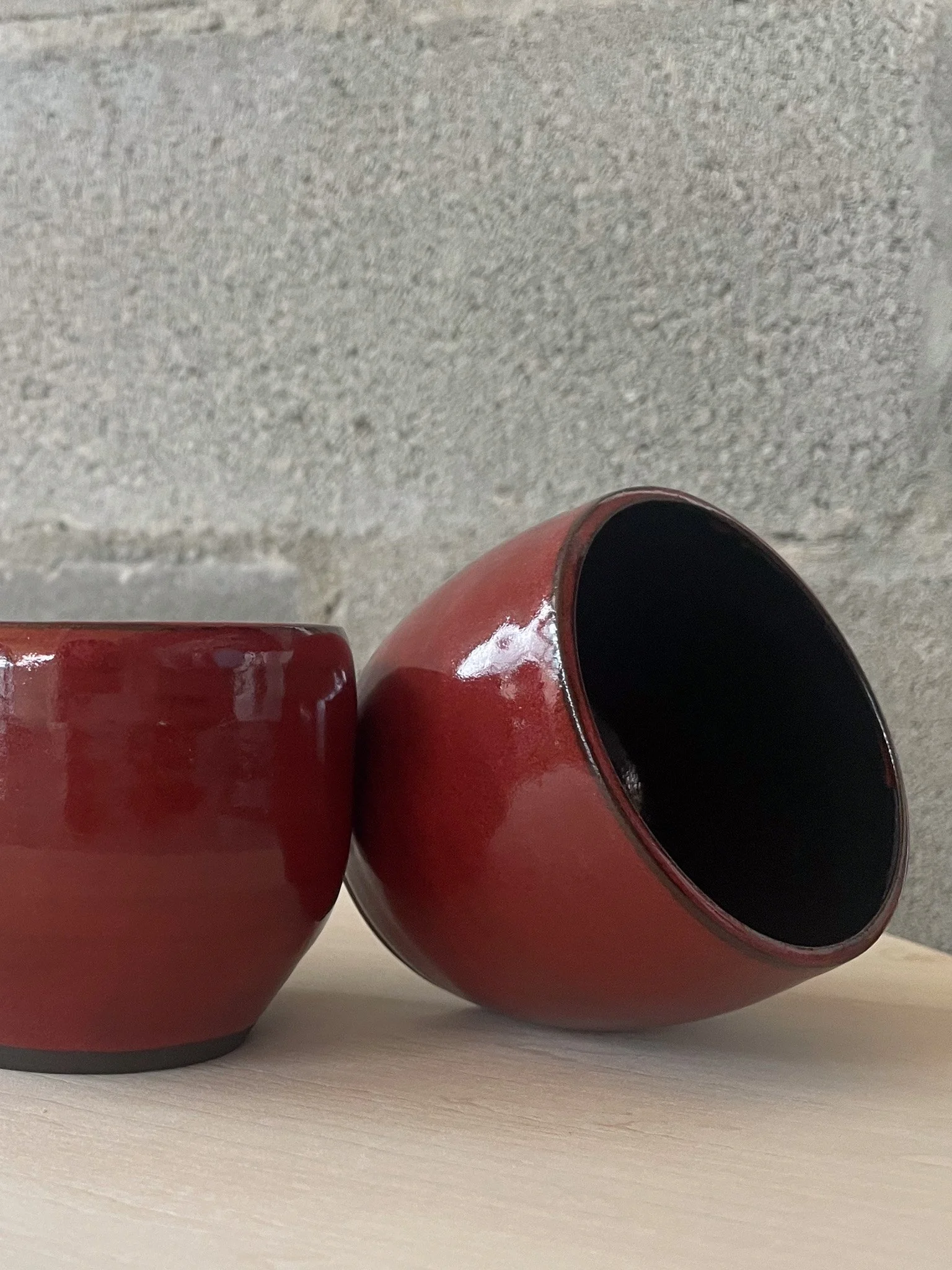 wheel-thrown stoneware cup in deep red with glossy black interior, Nordic rounded form
