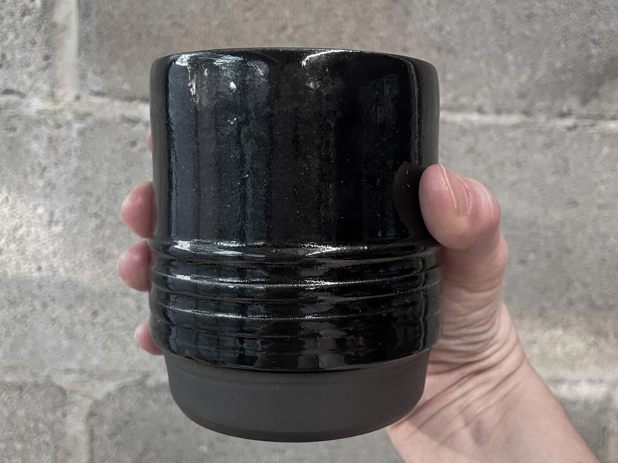 wheel-thrown stoneware coffee tumbler in glossy black glaze, brutalist ribbed form