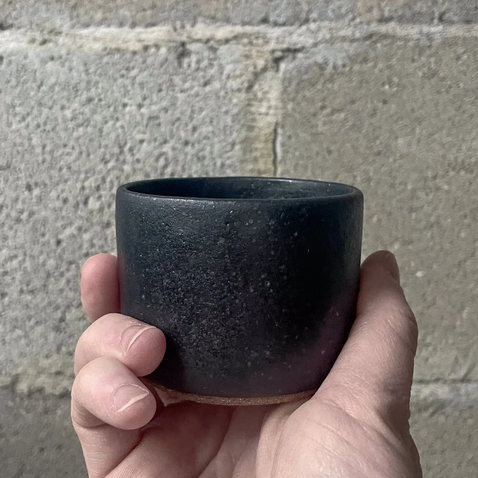 wheel-thrown stoneware cup in matte black glaze, brutalist minimal form