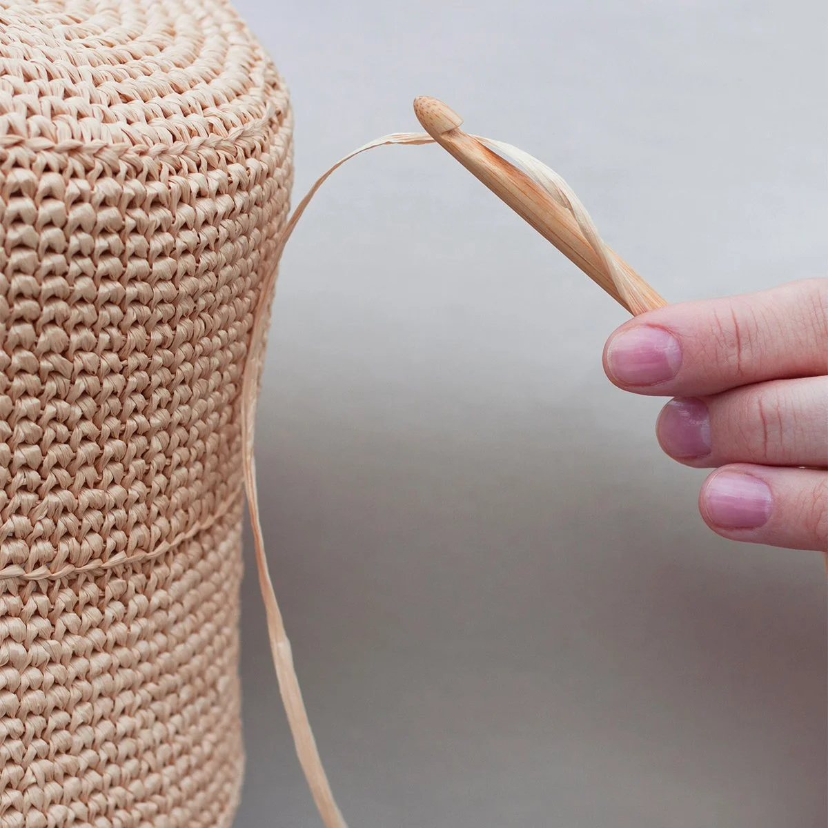 Person using a wooden crochet hook to make a woven basket from natural fibers.
