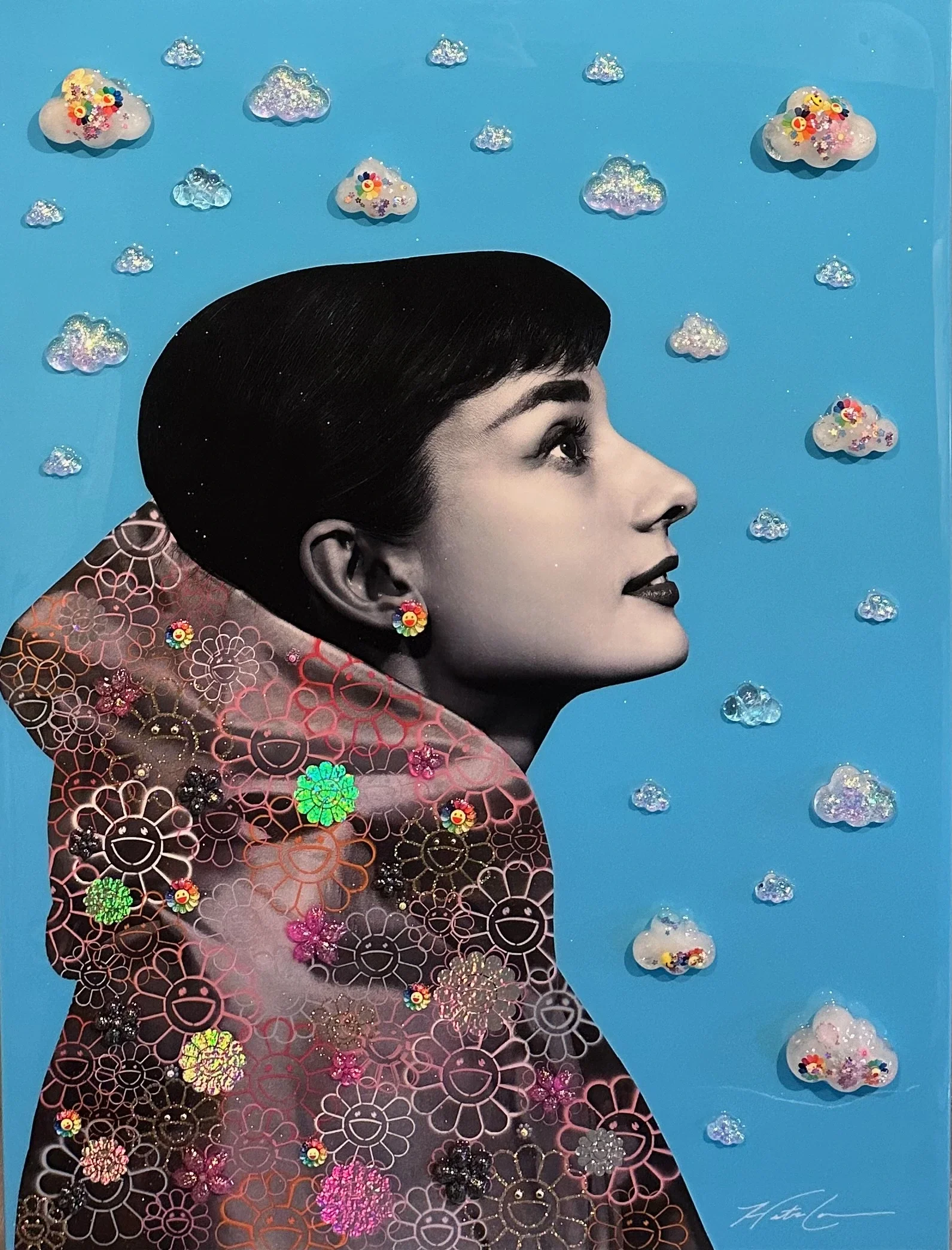 A profile of a Audrey Hepburn with dark hair against a blue background with glittery clouds and small, shiny, colorful decorative elements in the shape of flowers, smiley faces, and stars.