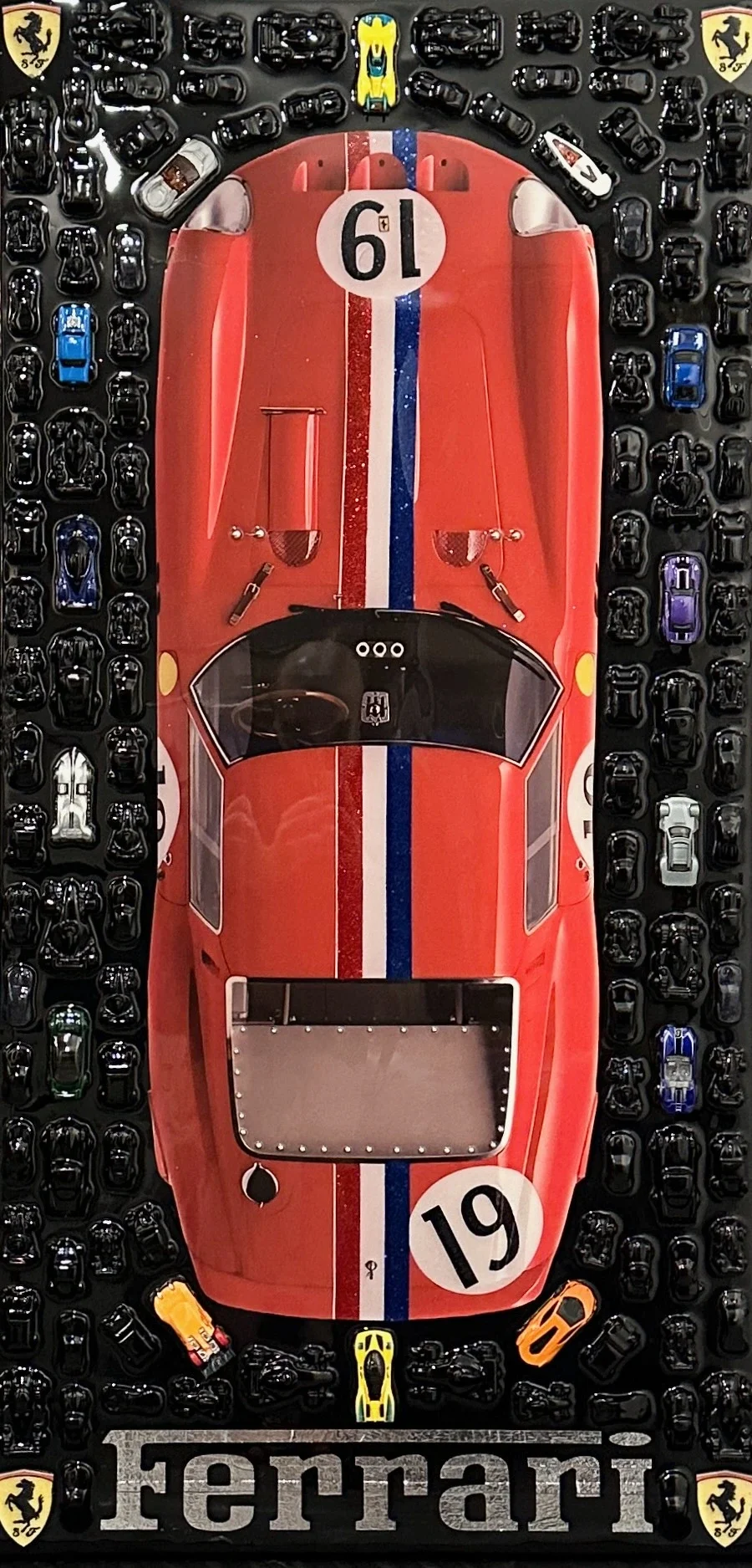 Top-down view of a red Ferrari race carith number 19, surrounded by various toy cars, placed on a display with Ferrari branding and shields.