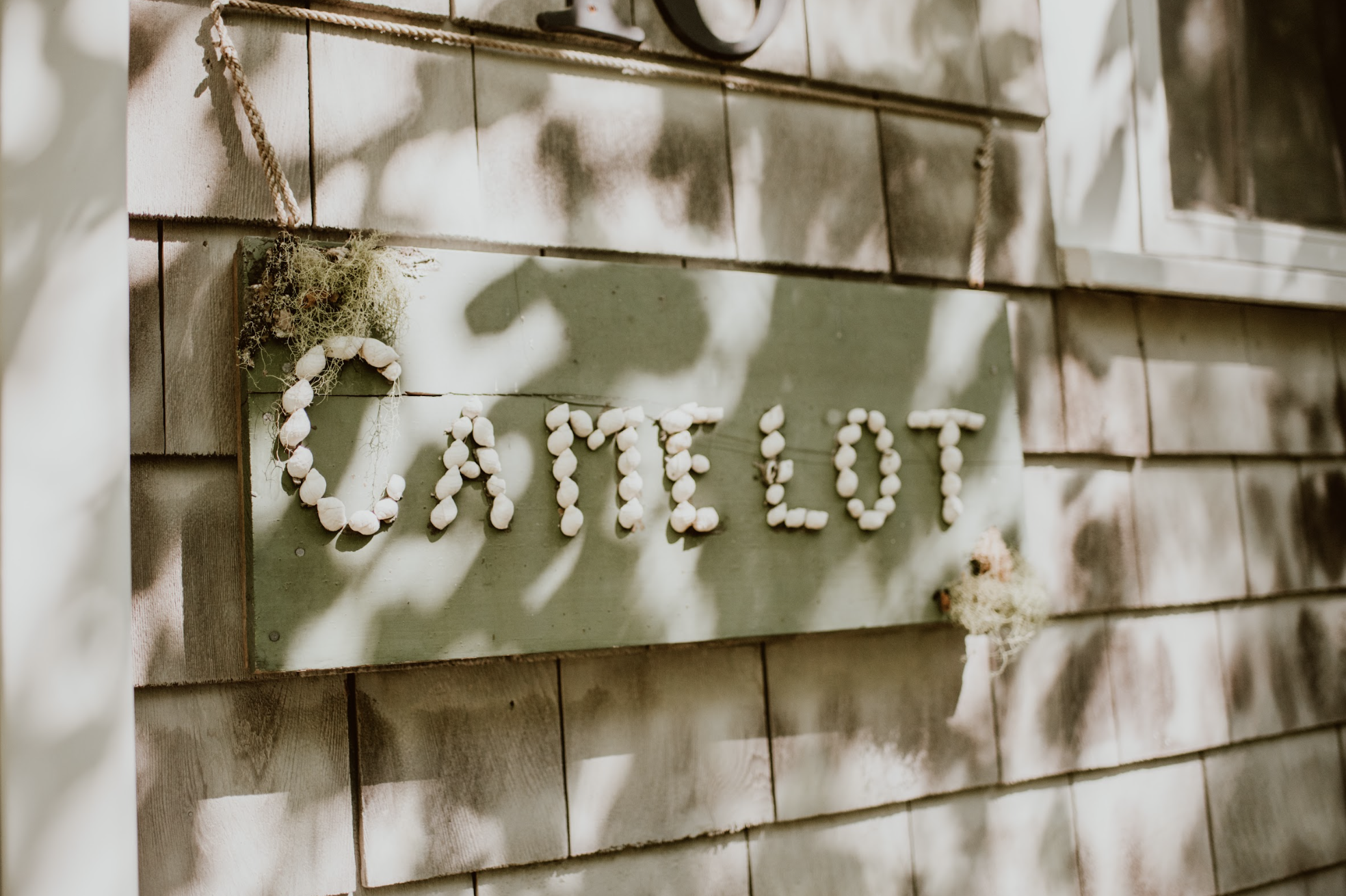 A wooden sign with the word 'CAMELOT' spelled out using small white shells.