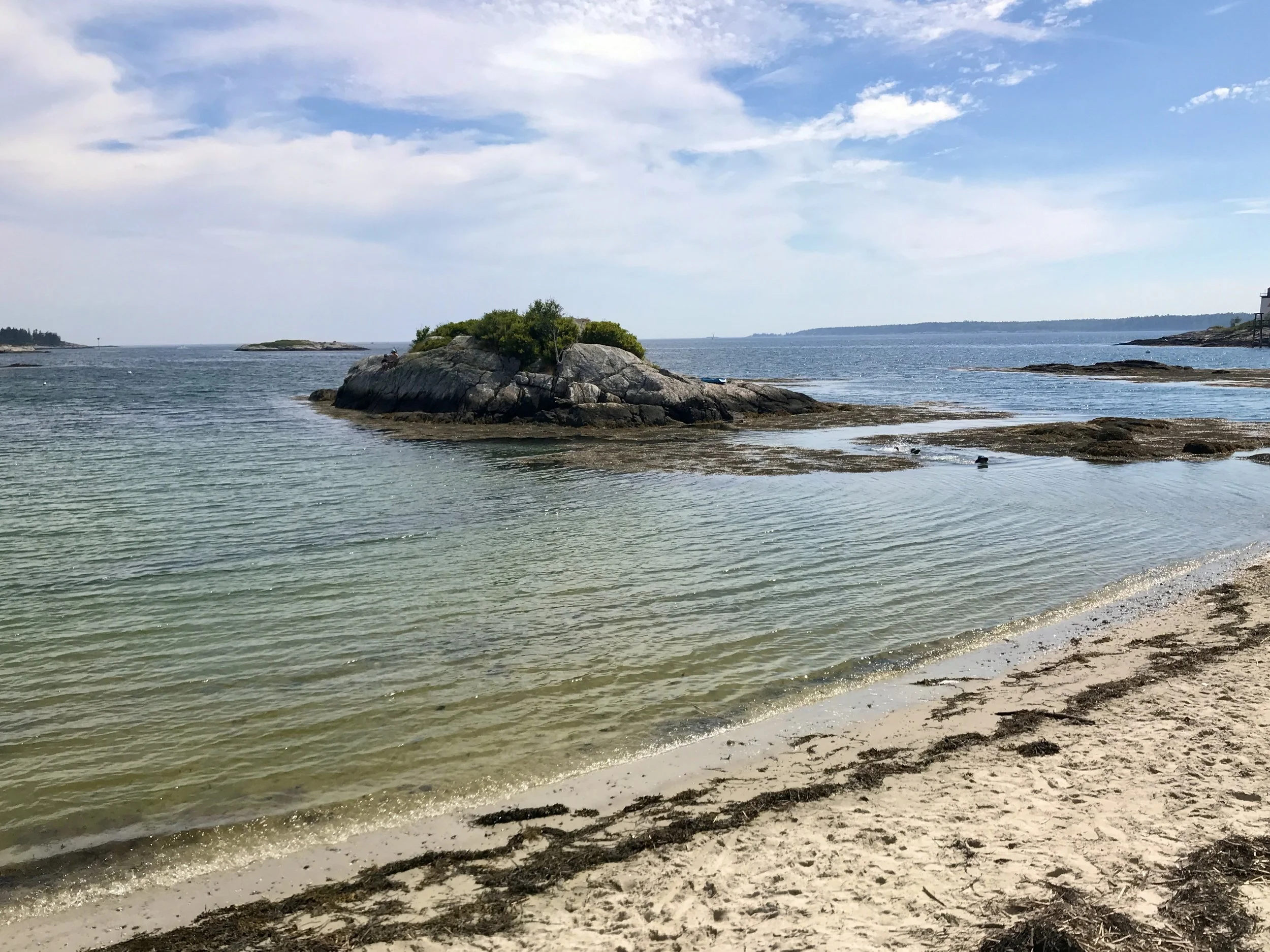 Calm beach with rocky islands and a sandy shore under a partly cloudy sky.