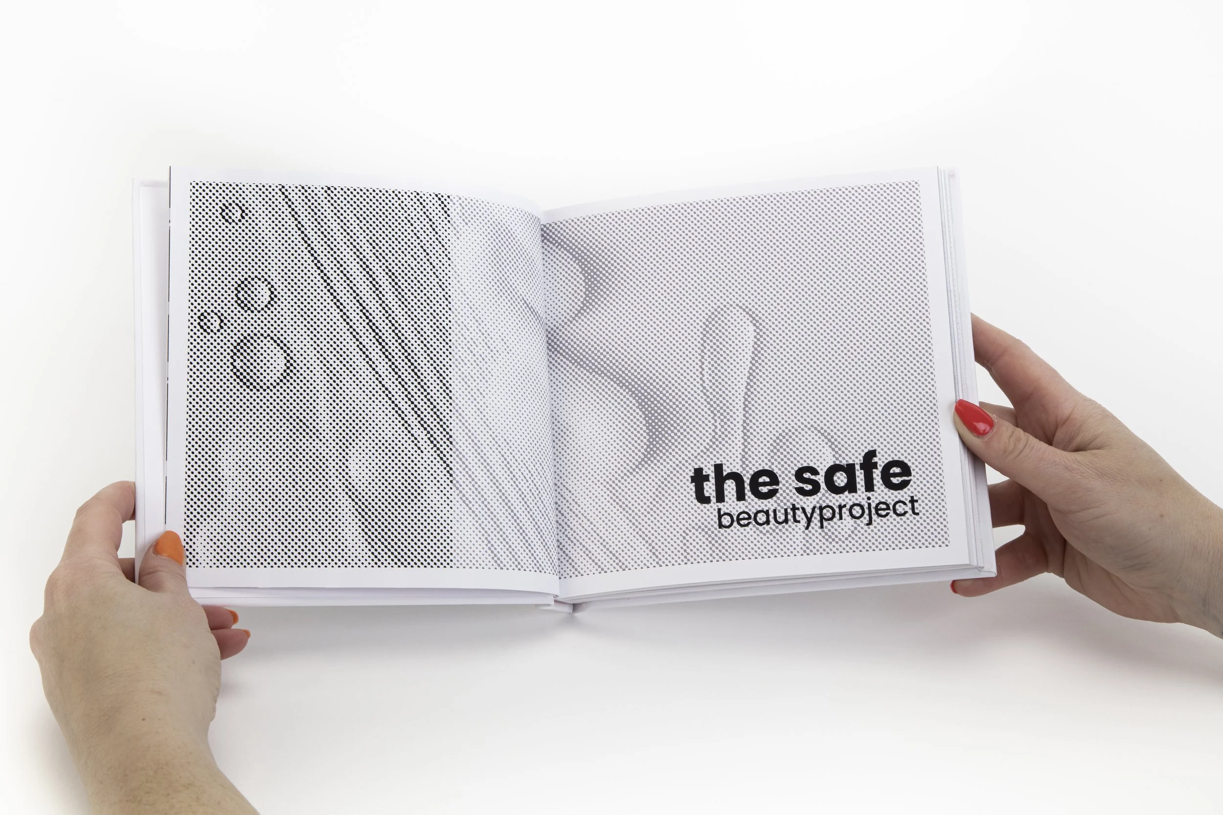 Open book with black and white halftone images and bold text that reads 'the safe beautyporject', held by two hands with painted nails.