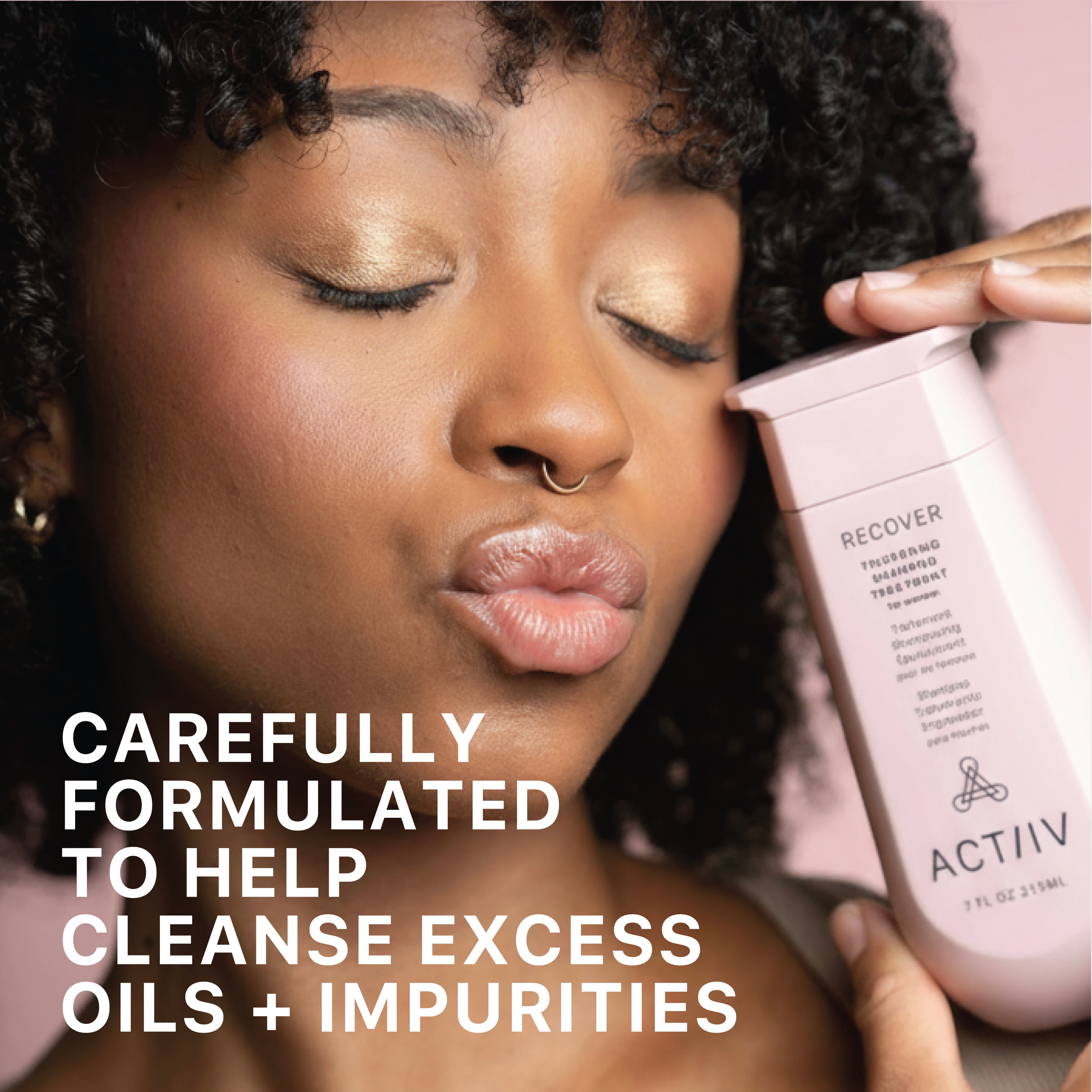 A woman with natural curly hair and makeup, holding a pink bottle labeled Active, close to her face. The bottle features the word Recover and a list of ingredients or benefits. The woman has her eyes closed and appears to be smelling or enjoying the product.