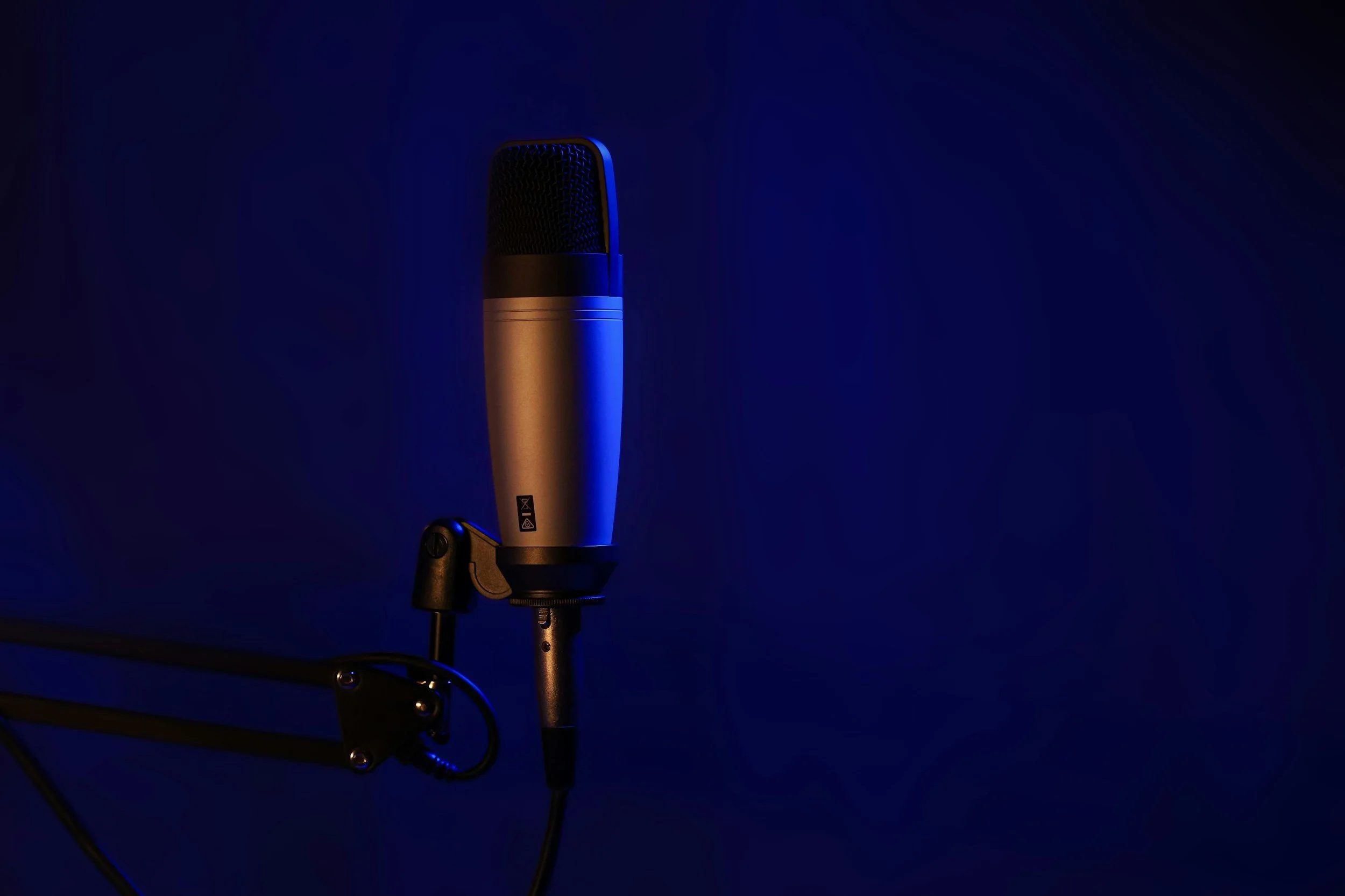 A professional studio microphone mounted on a black adjustable arm against a dark blue background.