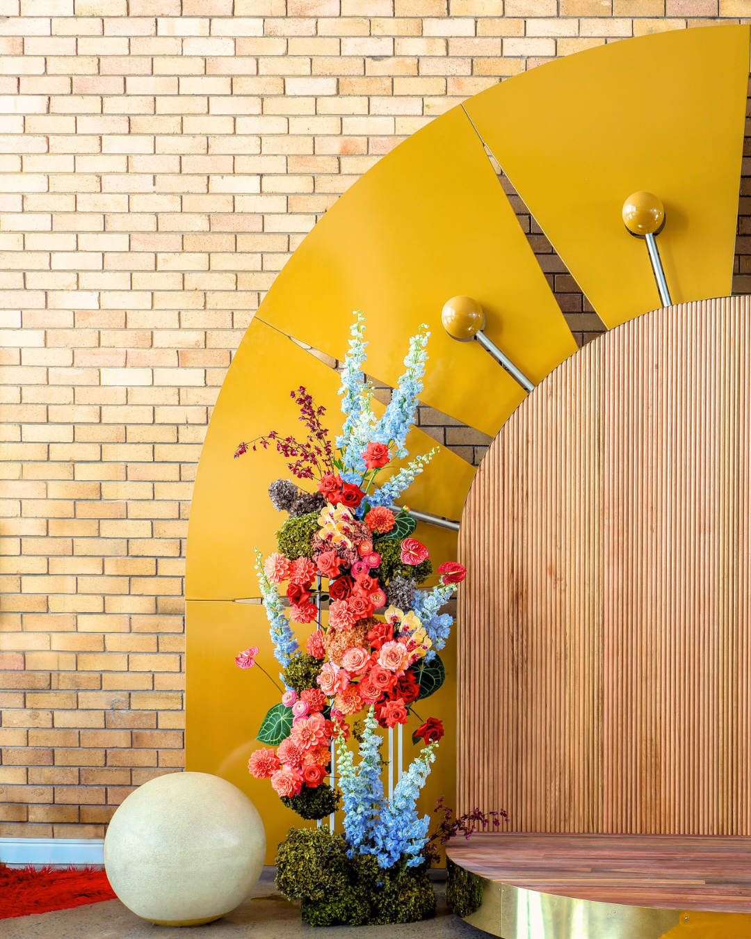 Decorative colorful flower arrangement next to a yellow and wood textured wall with a moon or sphere-shaped object nearby.