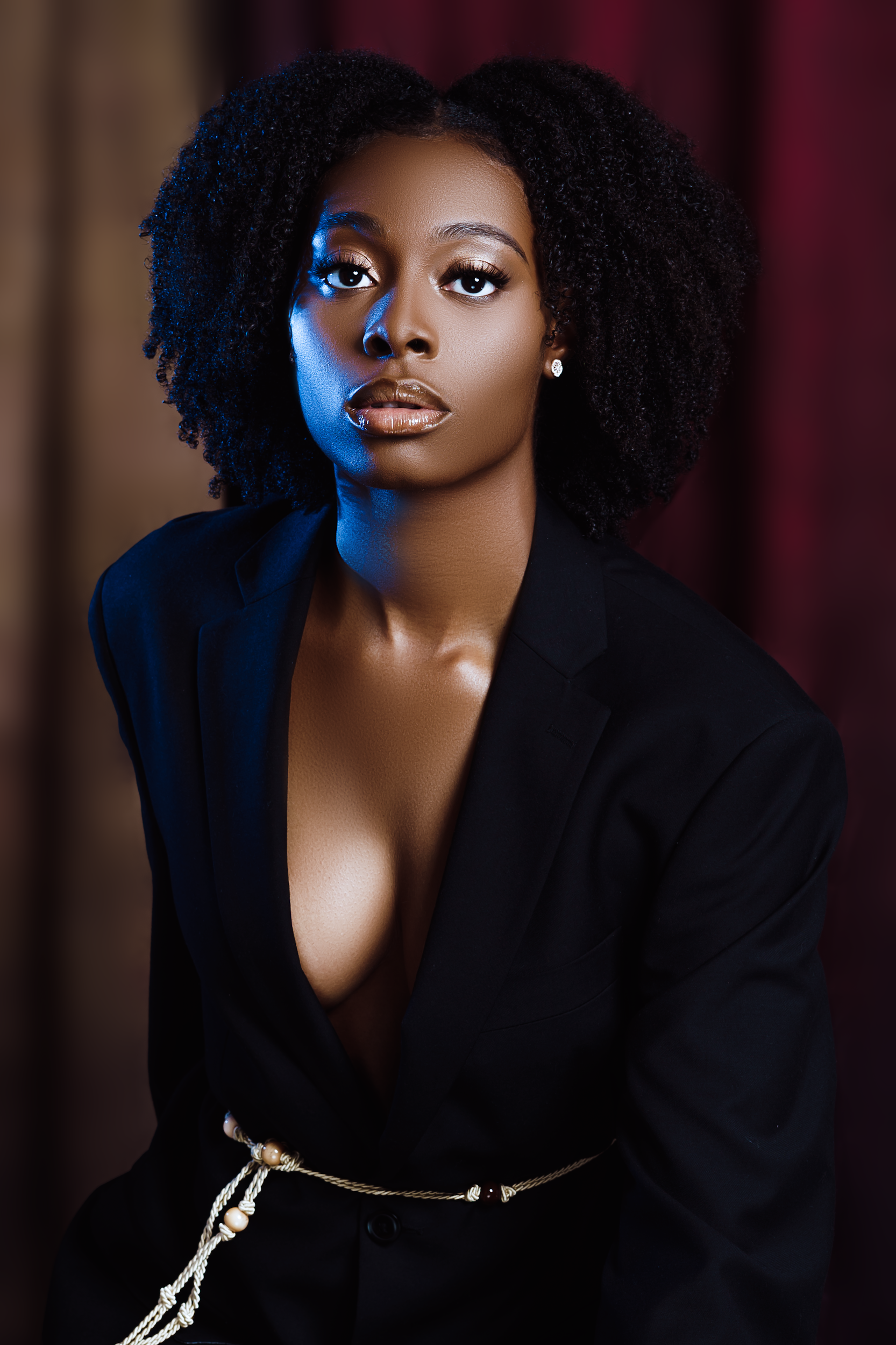 Close-up portrait of a powerful Black Woman with voluminous Ellevate Bold Coils™ hair, wearing a dark blazer. Her confident gaze and radiant complexion embody strength and the true essence of Black Beauty, Elevated.™ from Ellevate Beauty Montreal™.