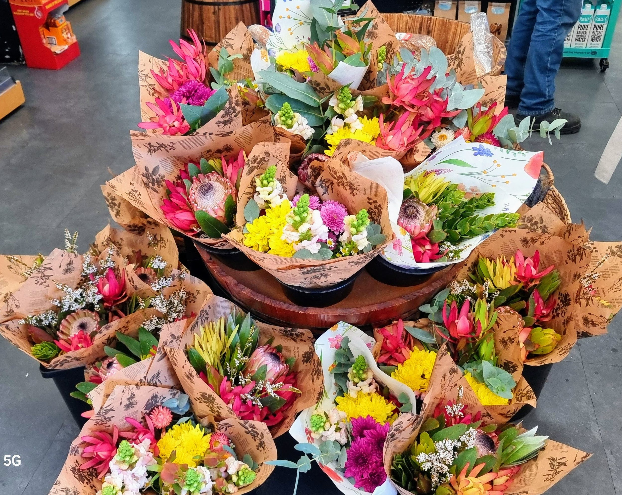 Multiple colorful flower bouquets wrapped in brown floral paper arranged on a display table in a store.