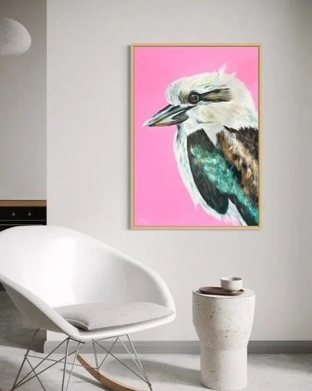 Painting of a kookaburra bird with a pink background hanging on a white wall in a modern room by Australian artist, Laura Boatman of Art By Boaty