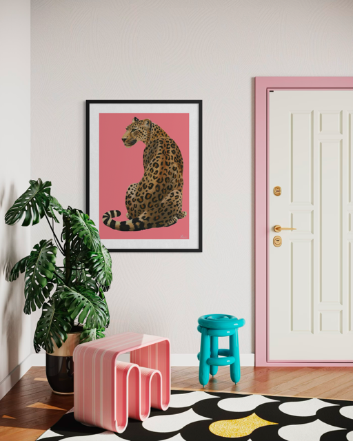 Interior of a room featuring a framed artwork of a sitting leopard on a pink background, a large houseplant with broad green leaves, a pink-striped child-sized chair, a small turquoise stool, and a door with pink trim.