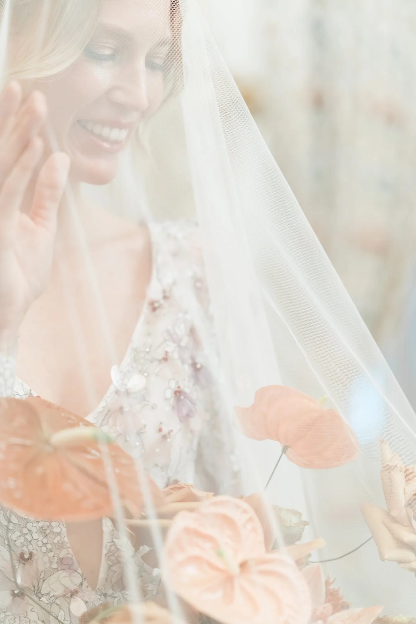 A bride smiling behind a veil, holding a bouquet of pink flowers.