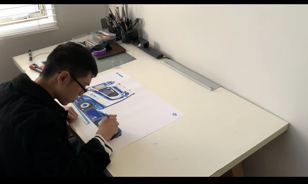 Designer Luq Turner at a white desk, working on a detailed illustration.