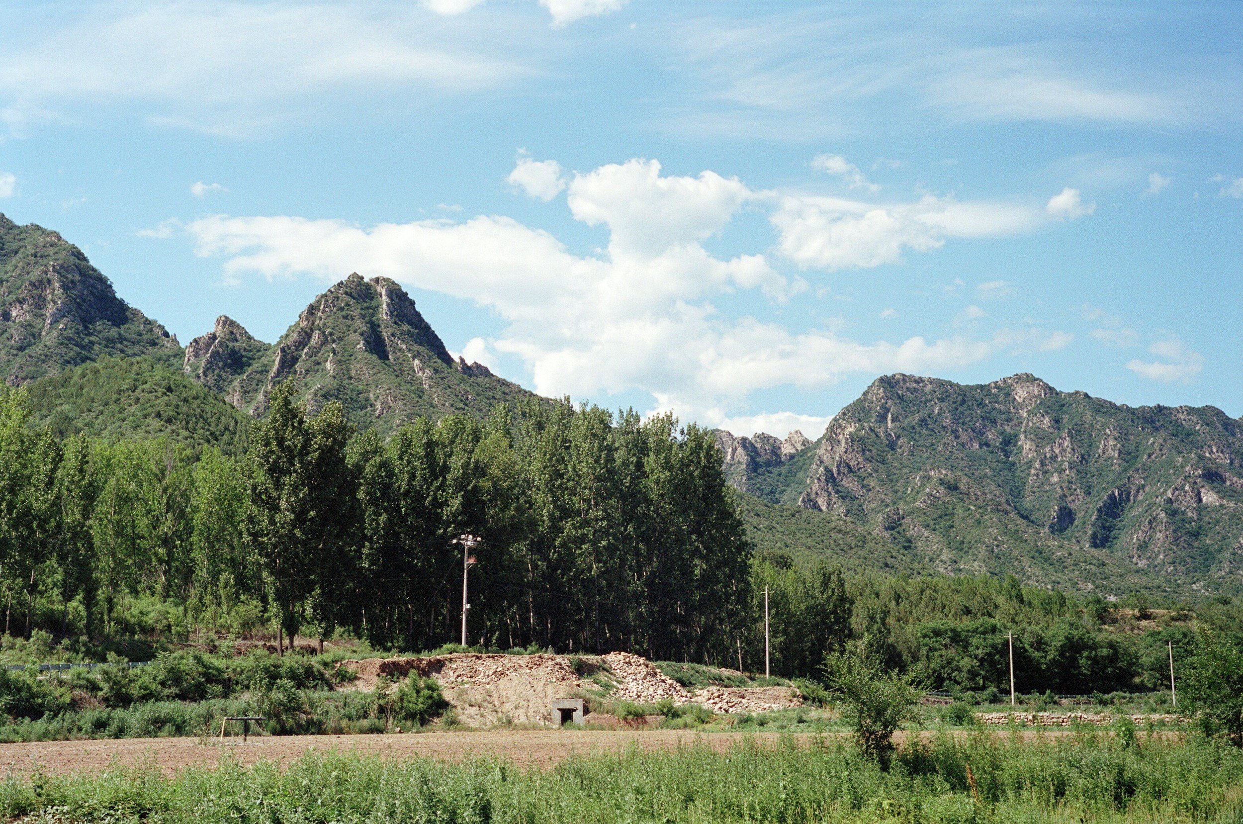 Scenic view of green mountains with a partly cloudy sky, trees, and fields in the foreground.