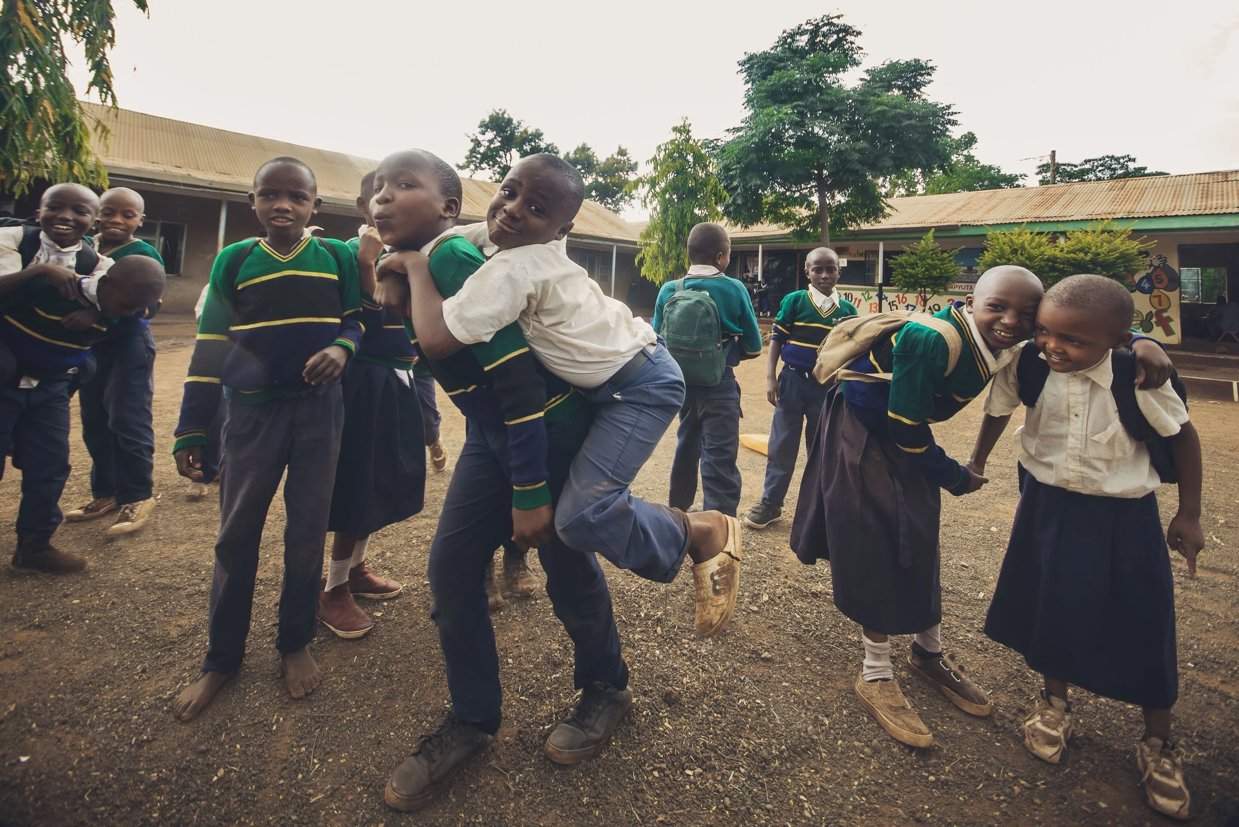 Group of school children playing outdoors, some pretending to be horse and rider, smiling and having fun, in a schoolyard.