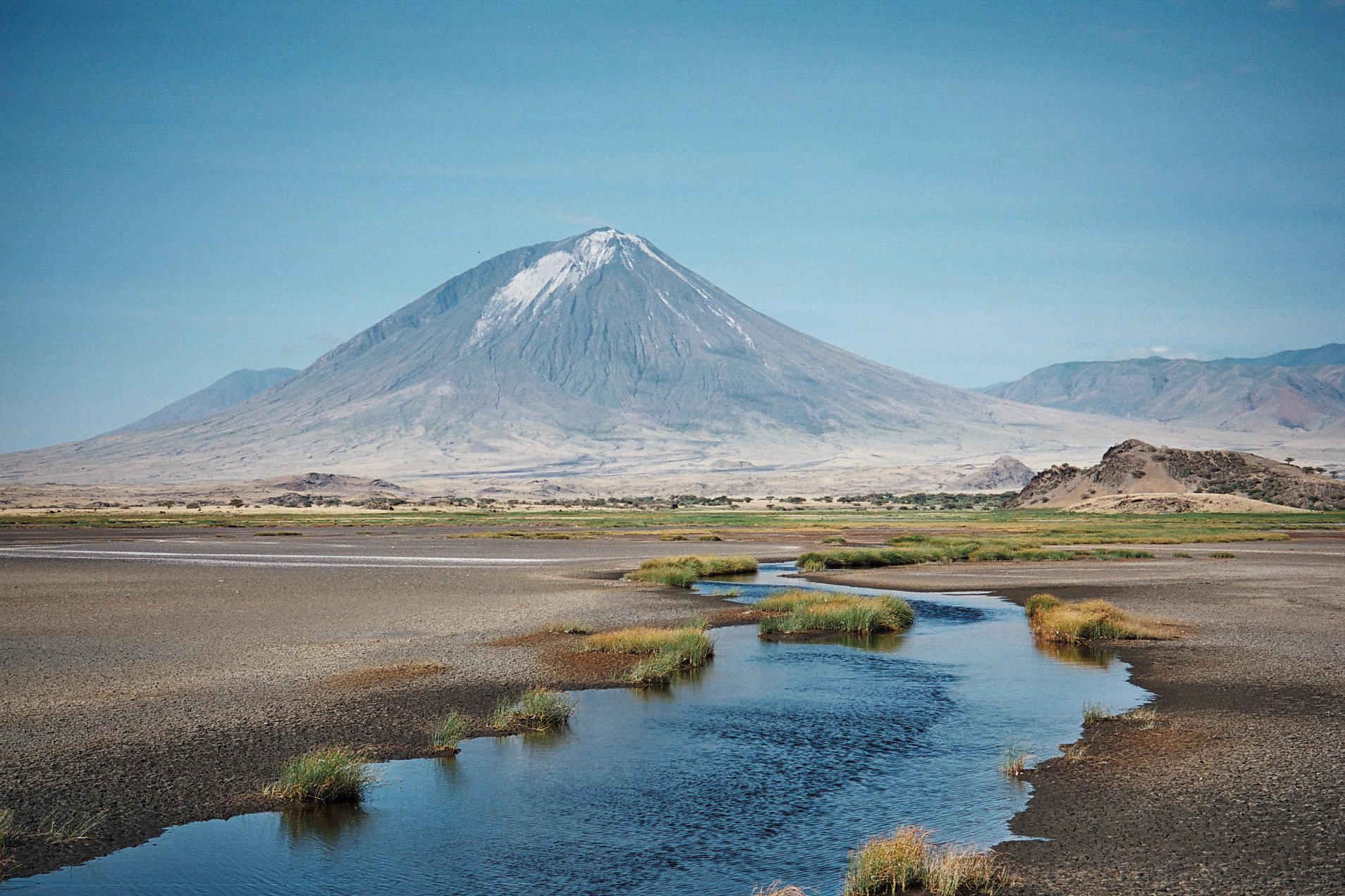 Scenic view of a volcanic mountain in the distance with a small stream flowing through the foreground across a dry plain.
